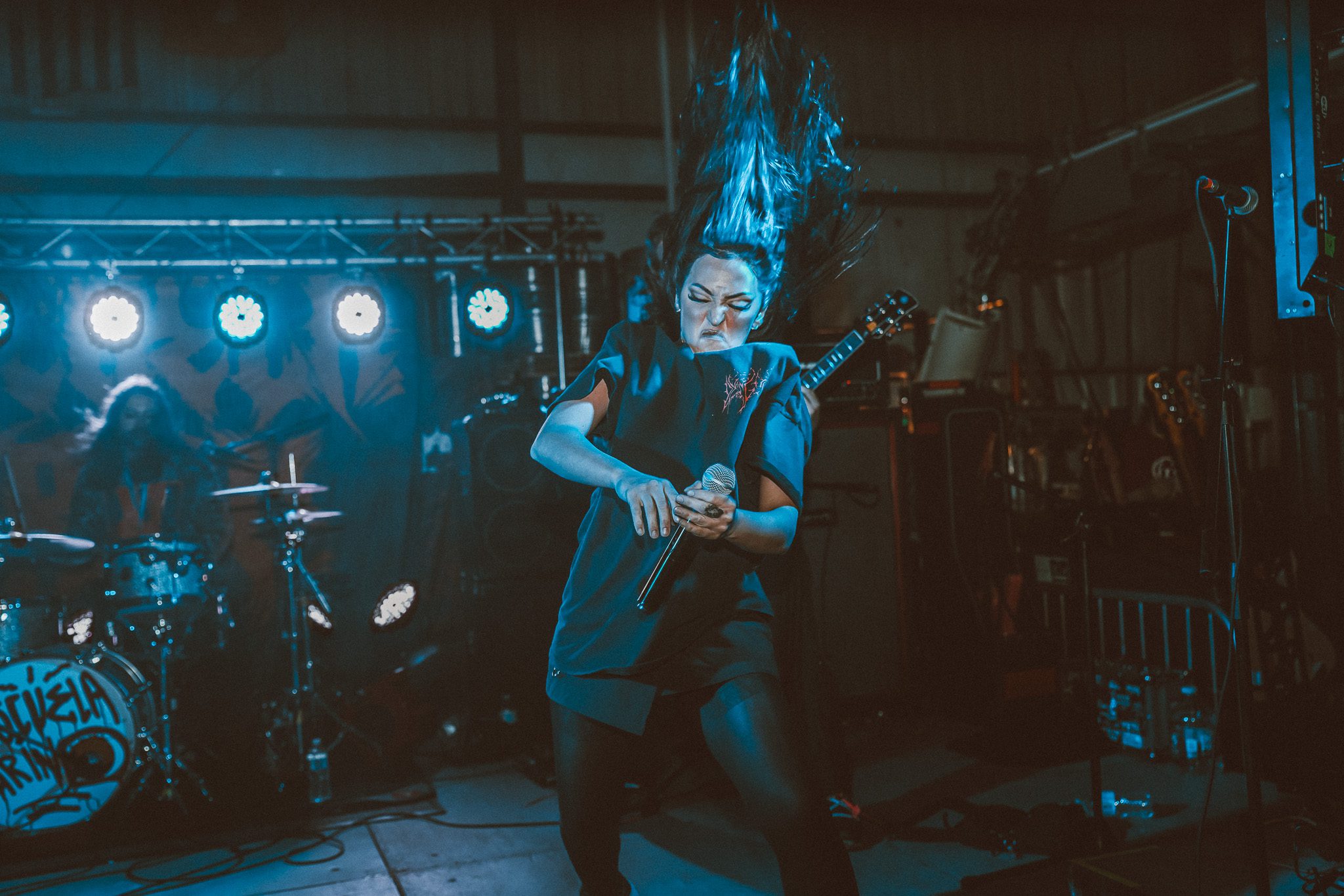 A group of five musicians posing together in a dimly lit space, with colorful lights and decorative vines in the background.