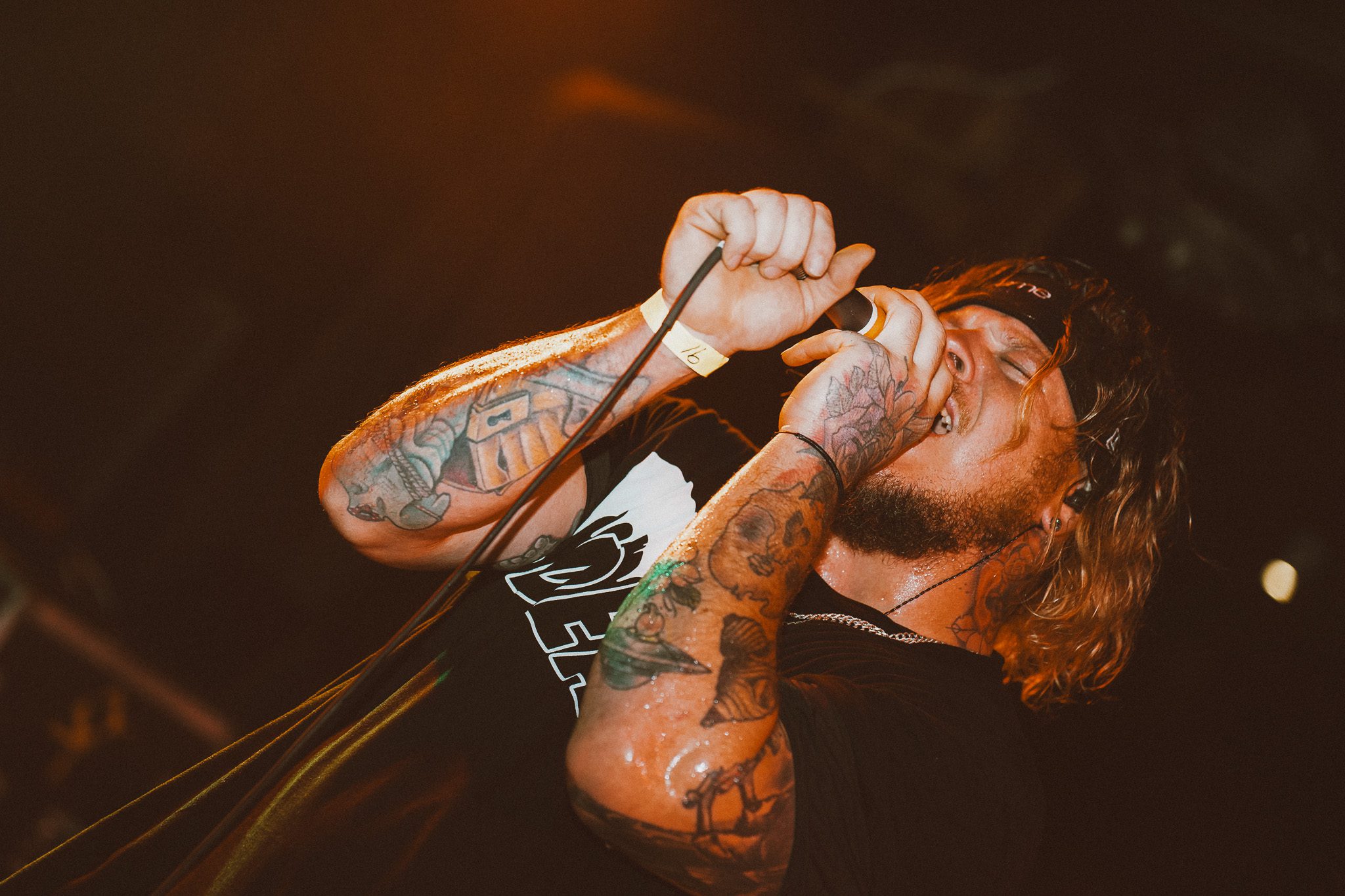 A musician playing a white electric guitar on stage, illuminated by green lights.