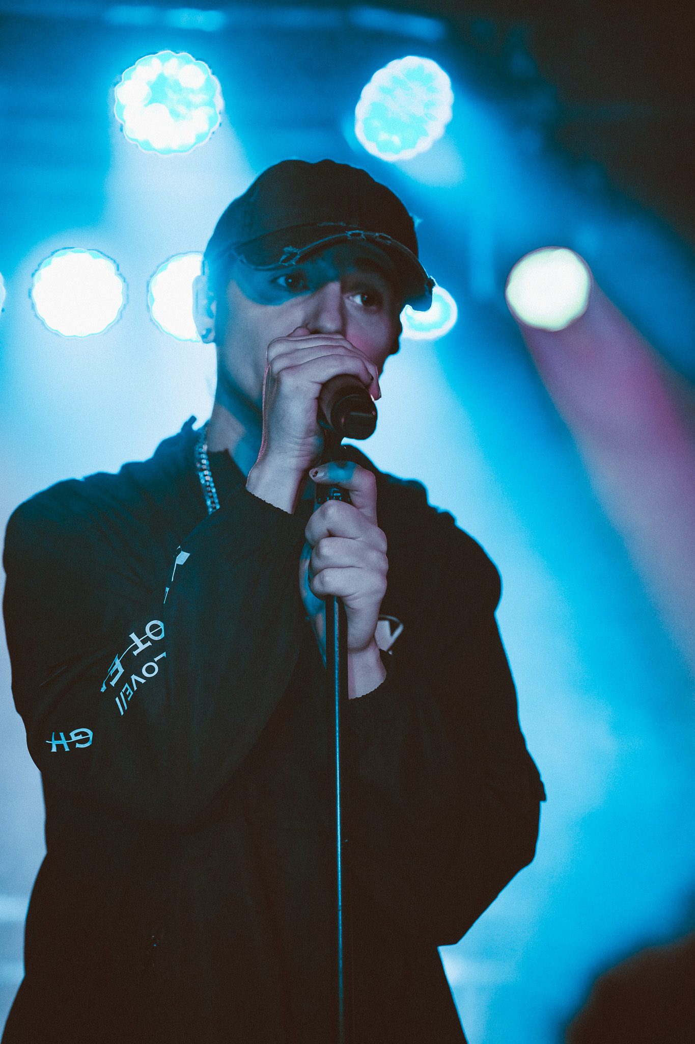 A drummer performing energetically on stage, smiling while playing a colorful drum set under green stage lights.