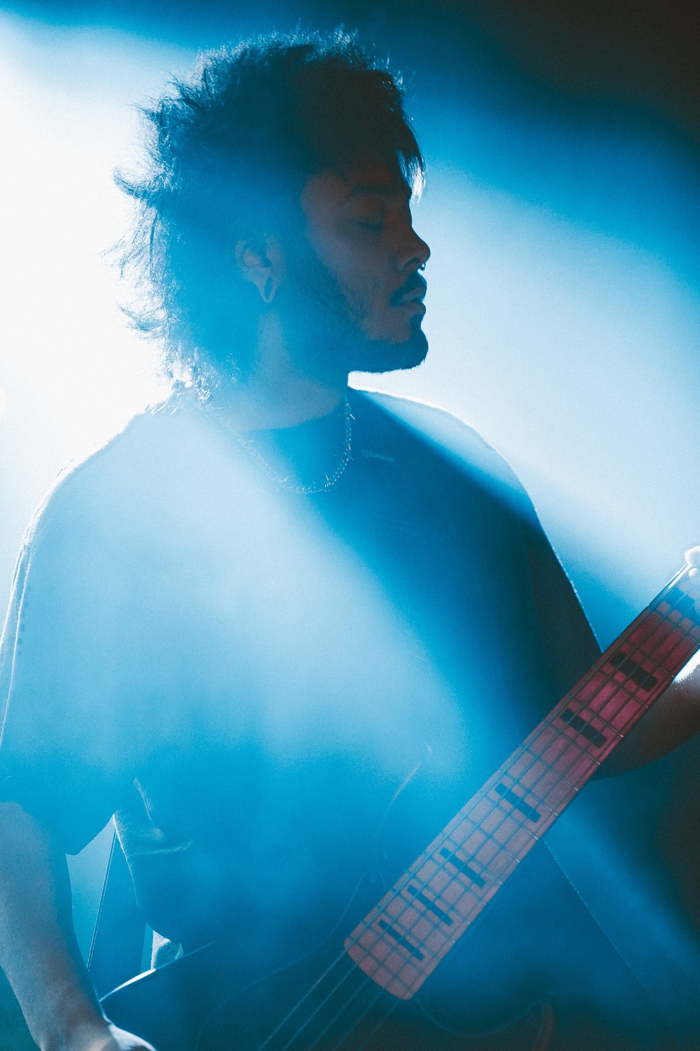A metal band performing on stage, with a bassist, guitarist, and drummer visible, under vibrant green lights.