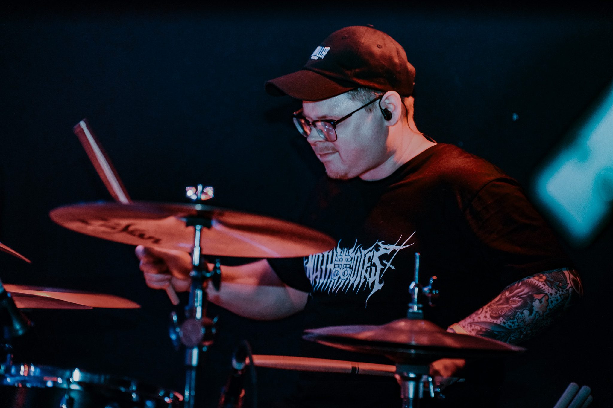 A guitarist with long hair performs passionately on stage, holding a bass guitar, set against colorful stage lighting.