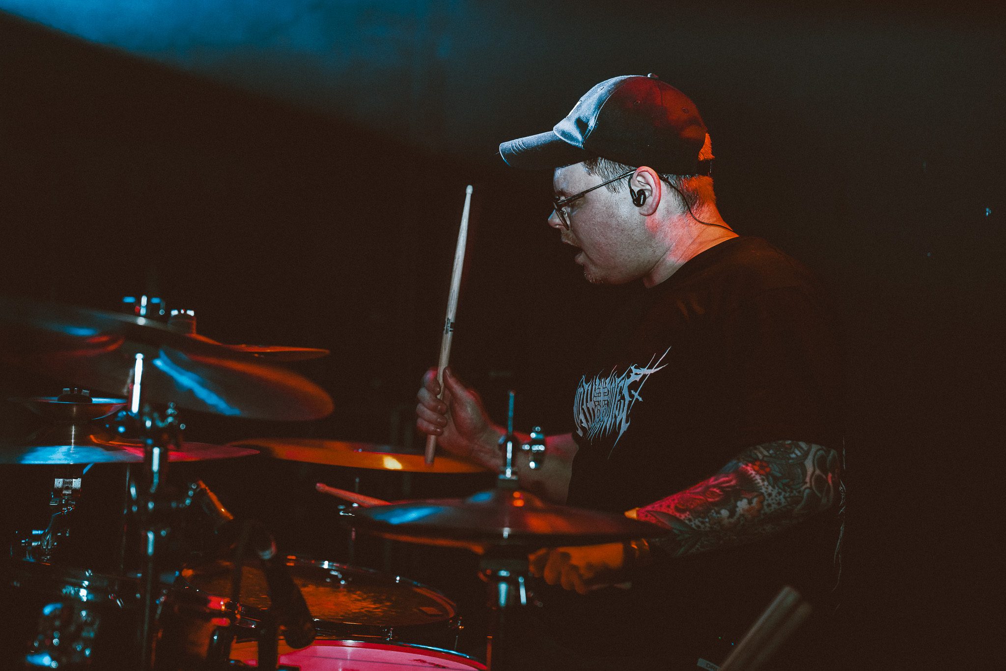 A crowd at a live metal concert with hands raised in a 'devil horns' gesture, illuminated by stage lights.