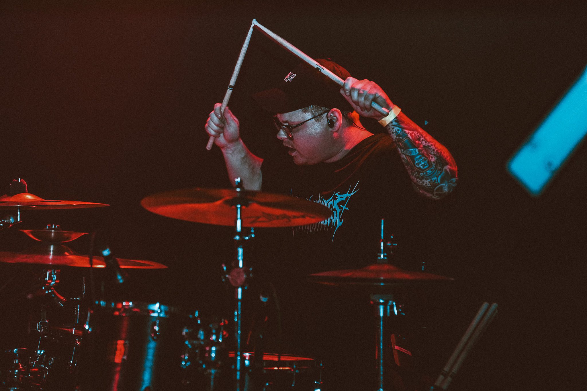 A male vocalist with tattoos passionately performing on stage, illuminated by dramatic lighting that creates a dynamic atmosphere.