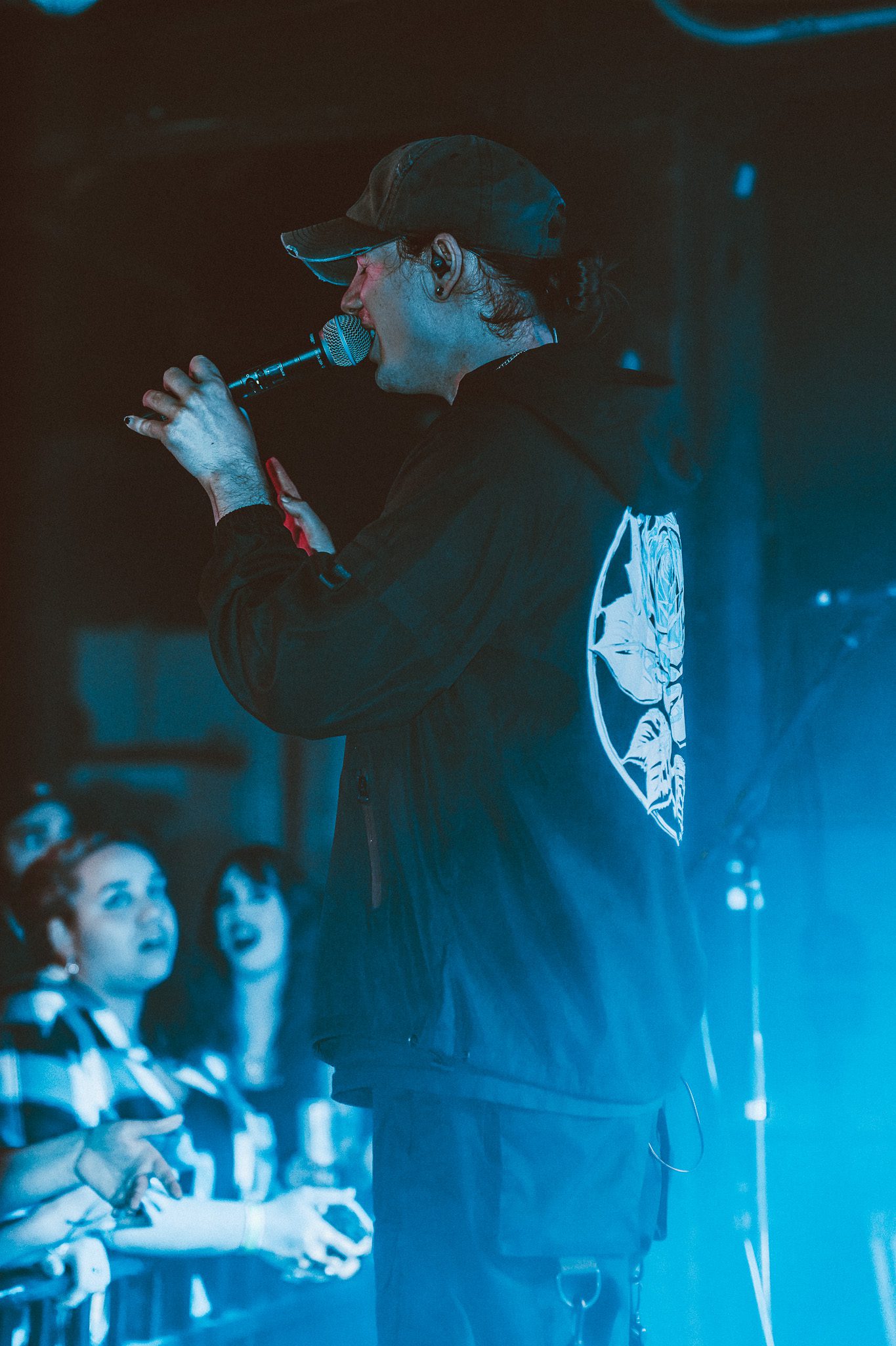 A guitarist passionately performing on stage with long hair, while a drummer plays in the background during a live music concert.