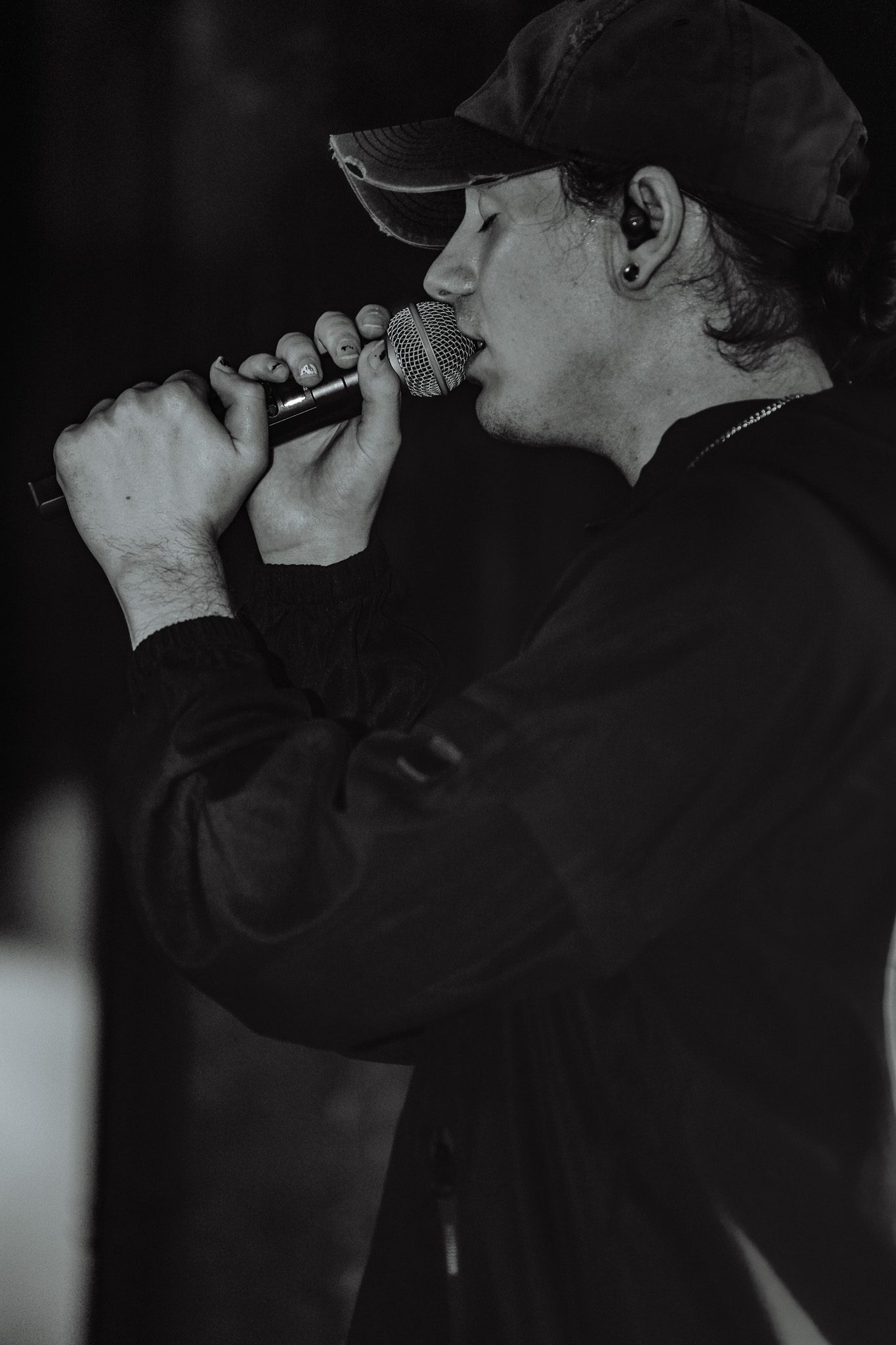Two guitarists in masks performing on stage during a metal concert, with a drum set and stage lights in the background.