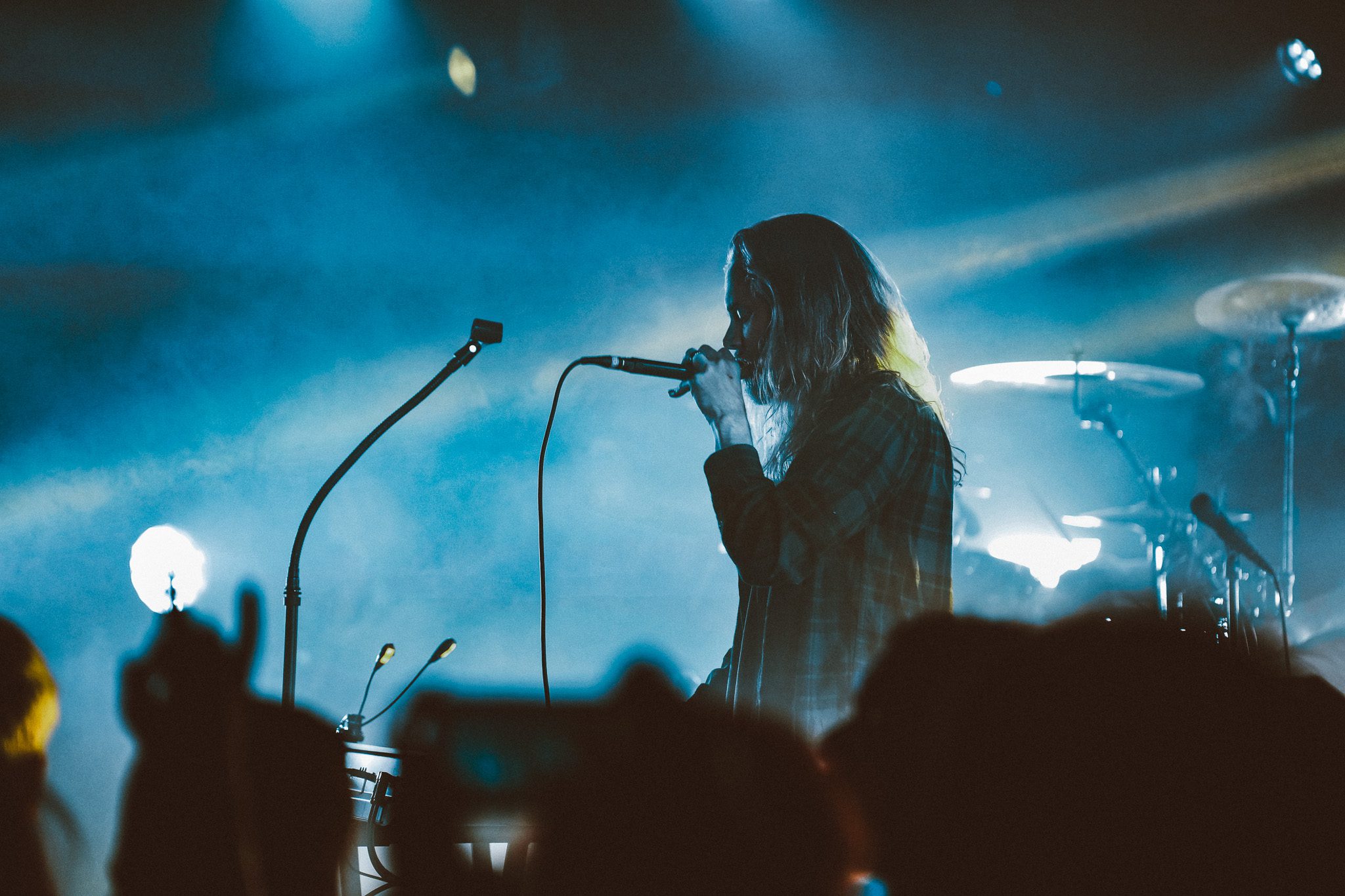 A metal band performing on stage, with one guitarist standing on an elevated platform and another bassist playing intensely, surrounded by stage lights and equipment.