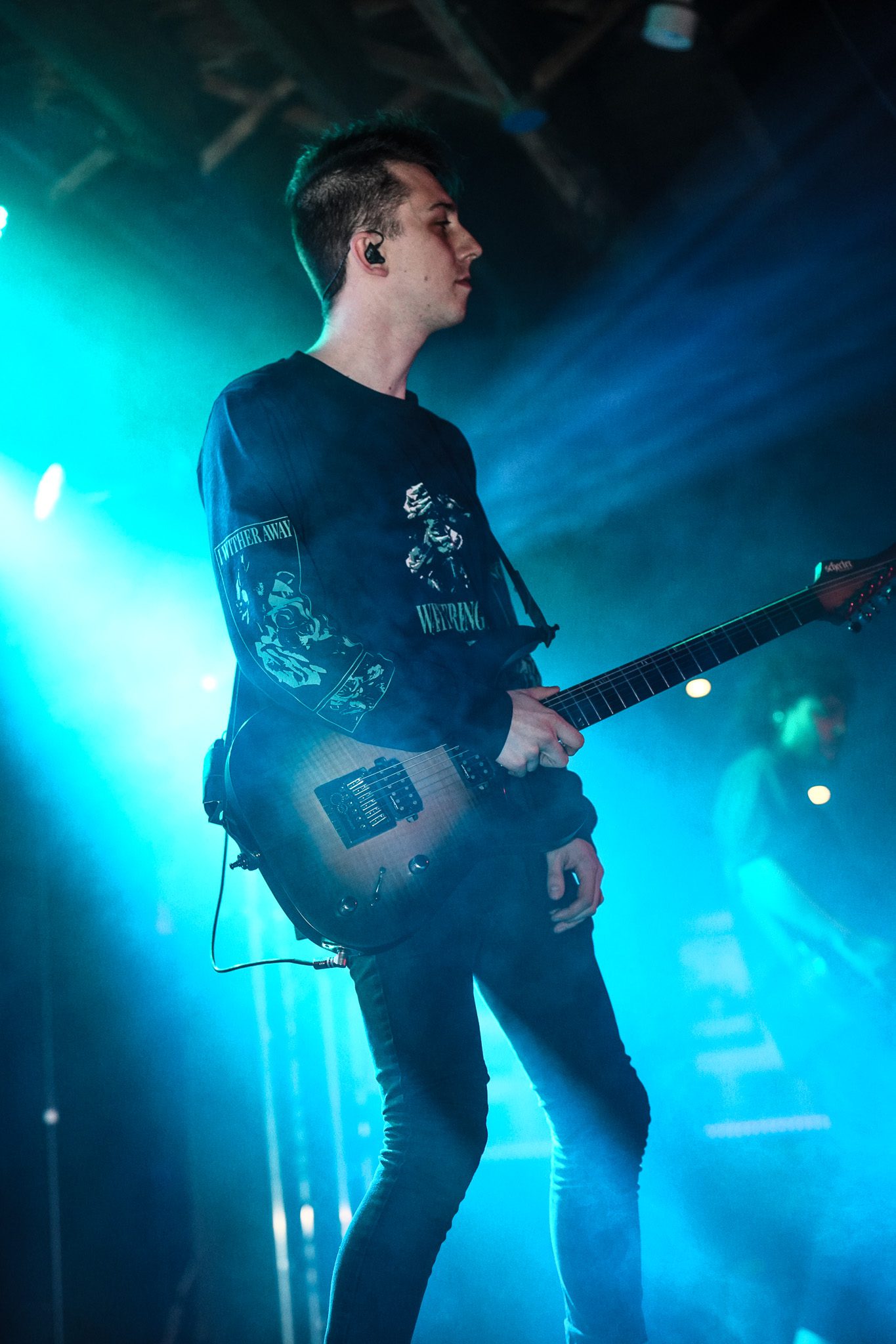 Two musicians performing on stage during a concert, one playing a guitar and the other playing a bass guitar, with dramatic lighting and visuals in the background.