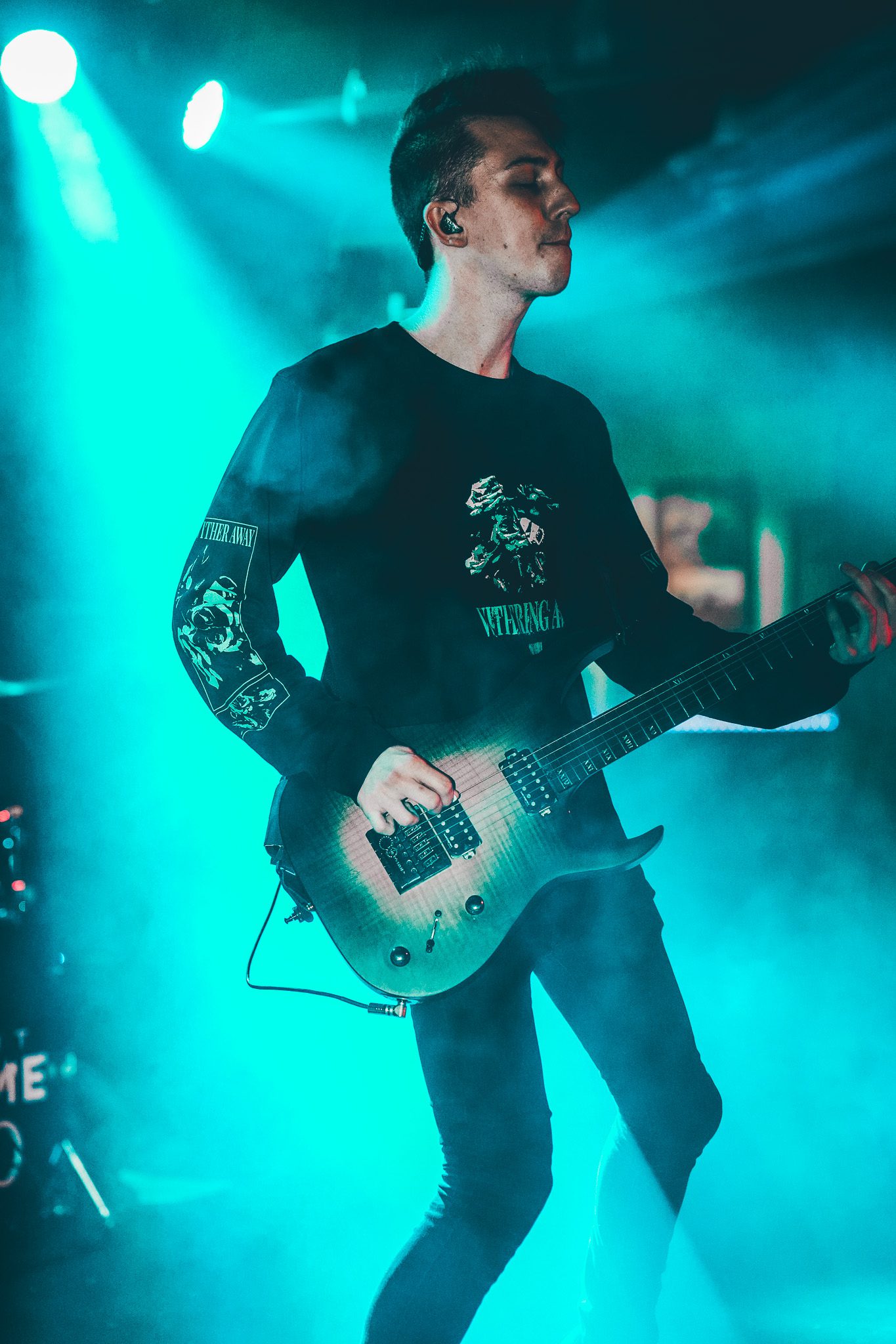 Musician performing on stage with a bass guitar during a live concert, illuminated by vibrant lights.