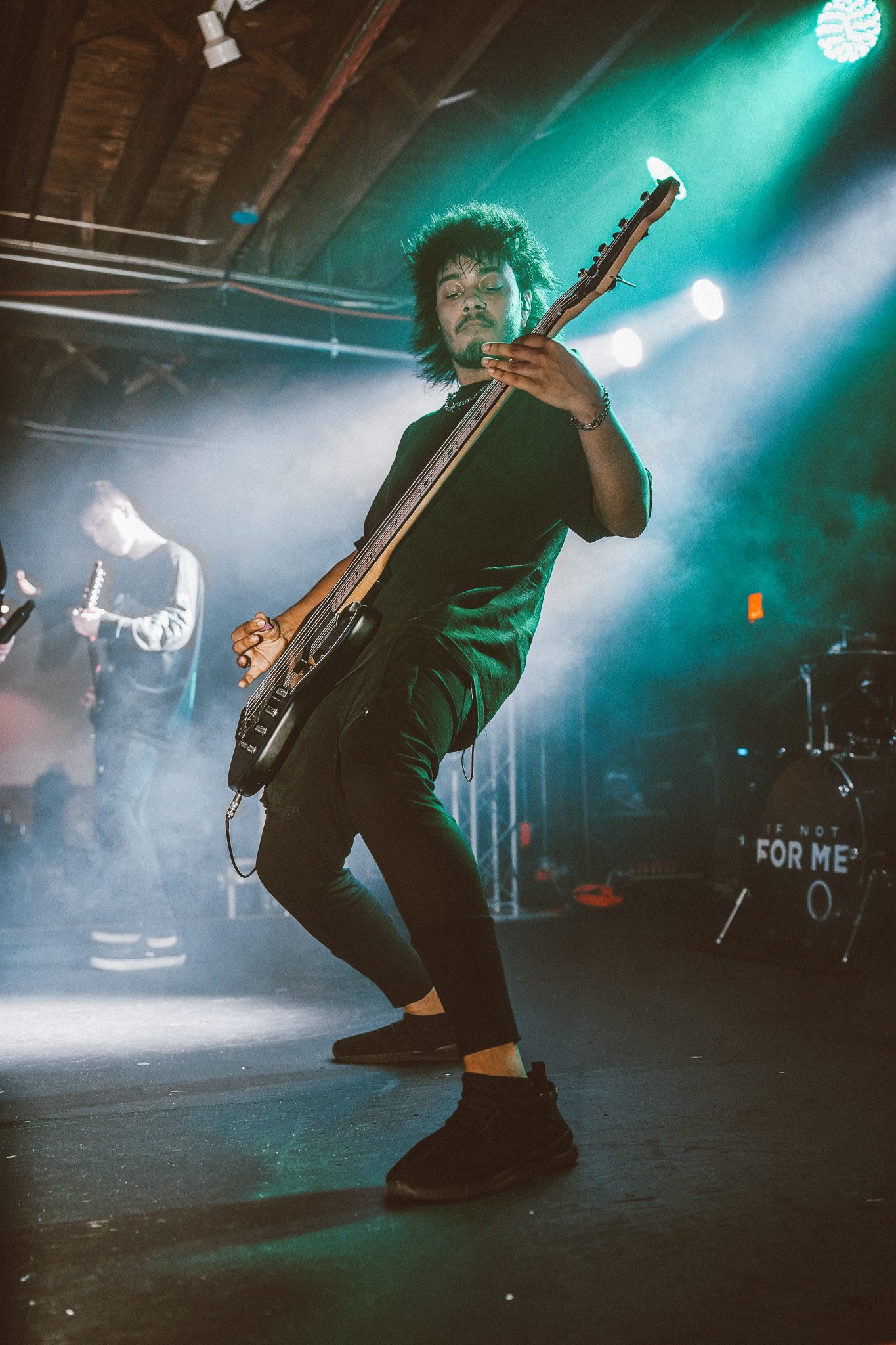 A metal band performs on stage in front of an energetic crowd, with bright stage lights and a backdrop featuring their logo.