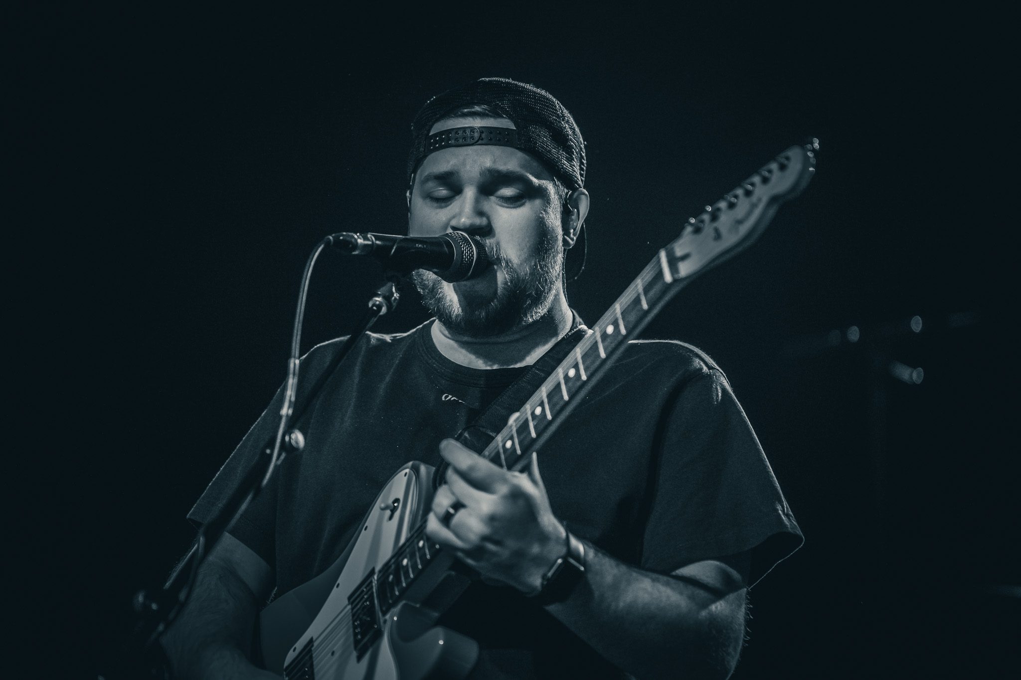 A musician performing passionately on stage, playing an electric guitar and singing into a microphone. The setting is illuminated with stage lights, creating a lively atmosphere.
