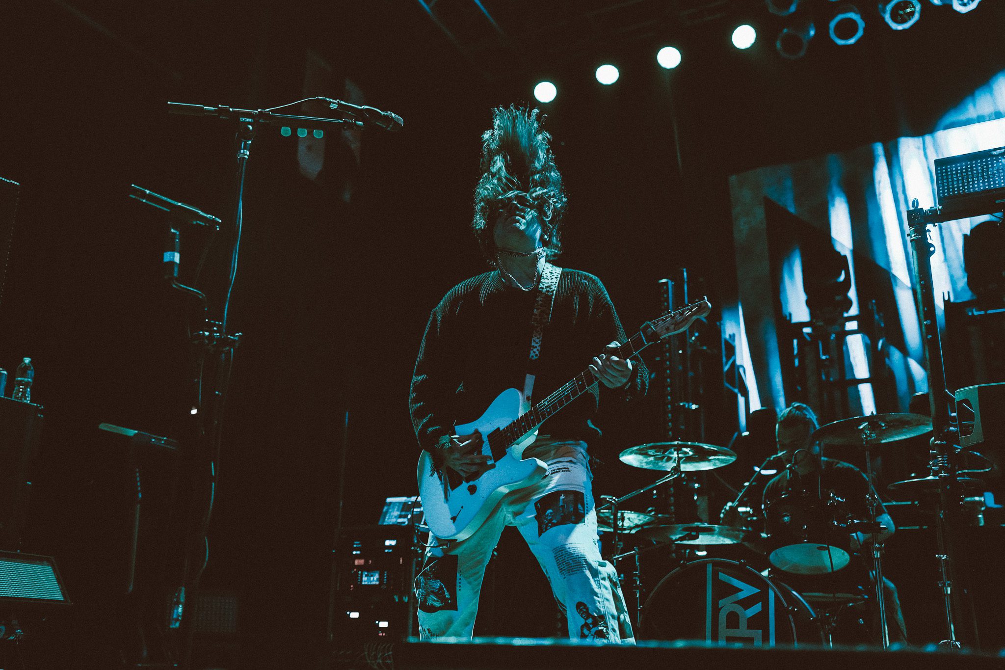 A musician playing an electric guitar on stage under warm stage lights, captured in a dynamic pose.