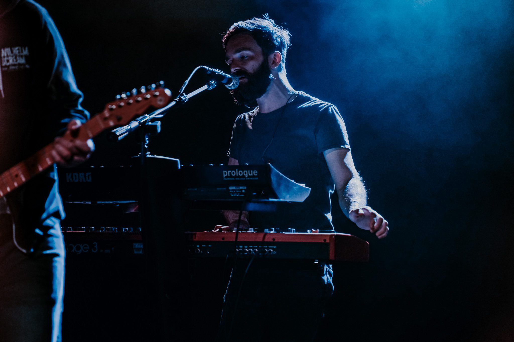 A guitarist performing on stage with a green electric guitar, focusing on the performance as vibrant stage lights illuminate the scene.