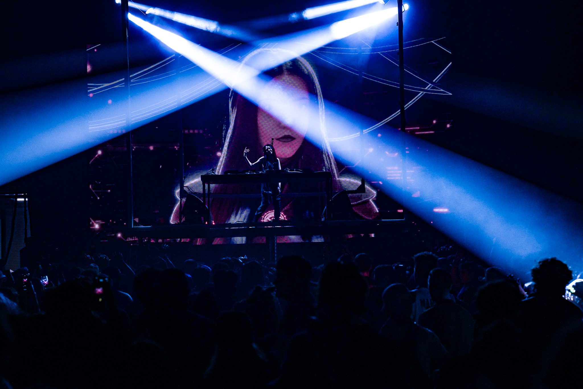 A singer with long hair performs on stage, holding a microphone with intense lighting creating a vibrant atmosphere.