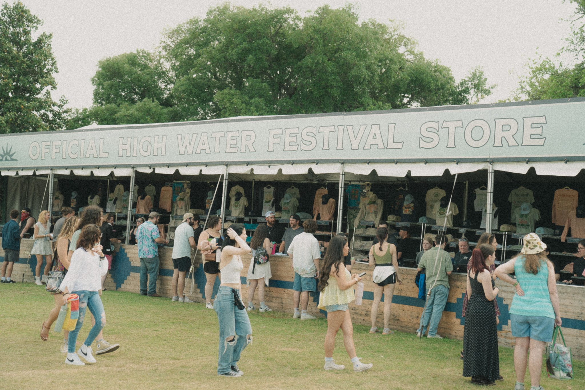 Crowd gathered in front of the official High Water Festival merchandise tent, with festival-goers browsing items for sale.