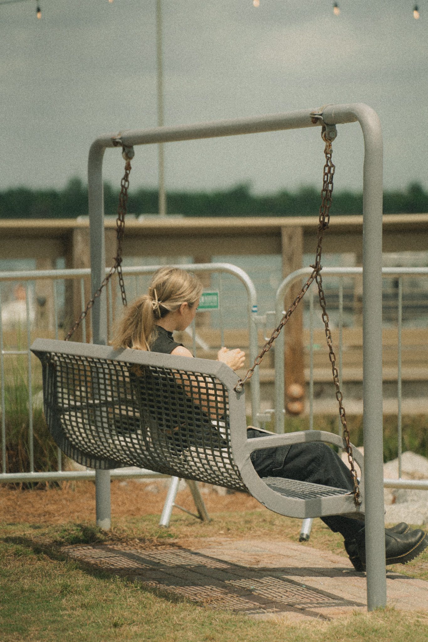 A person sitting on a swing at a festival, appearing relaxed and contemplative with the background showing a wooden railing and greenery.