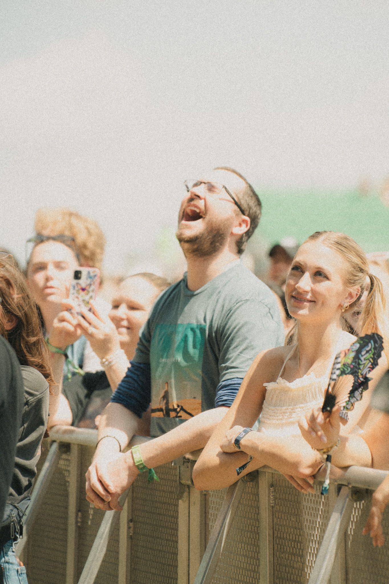 A crowd enjoying live music at a festival, with a man laughing energetically and a woman smiling nearby, surrounded by other attendees.