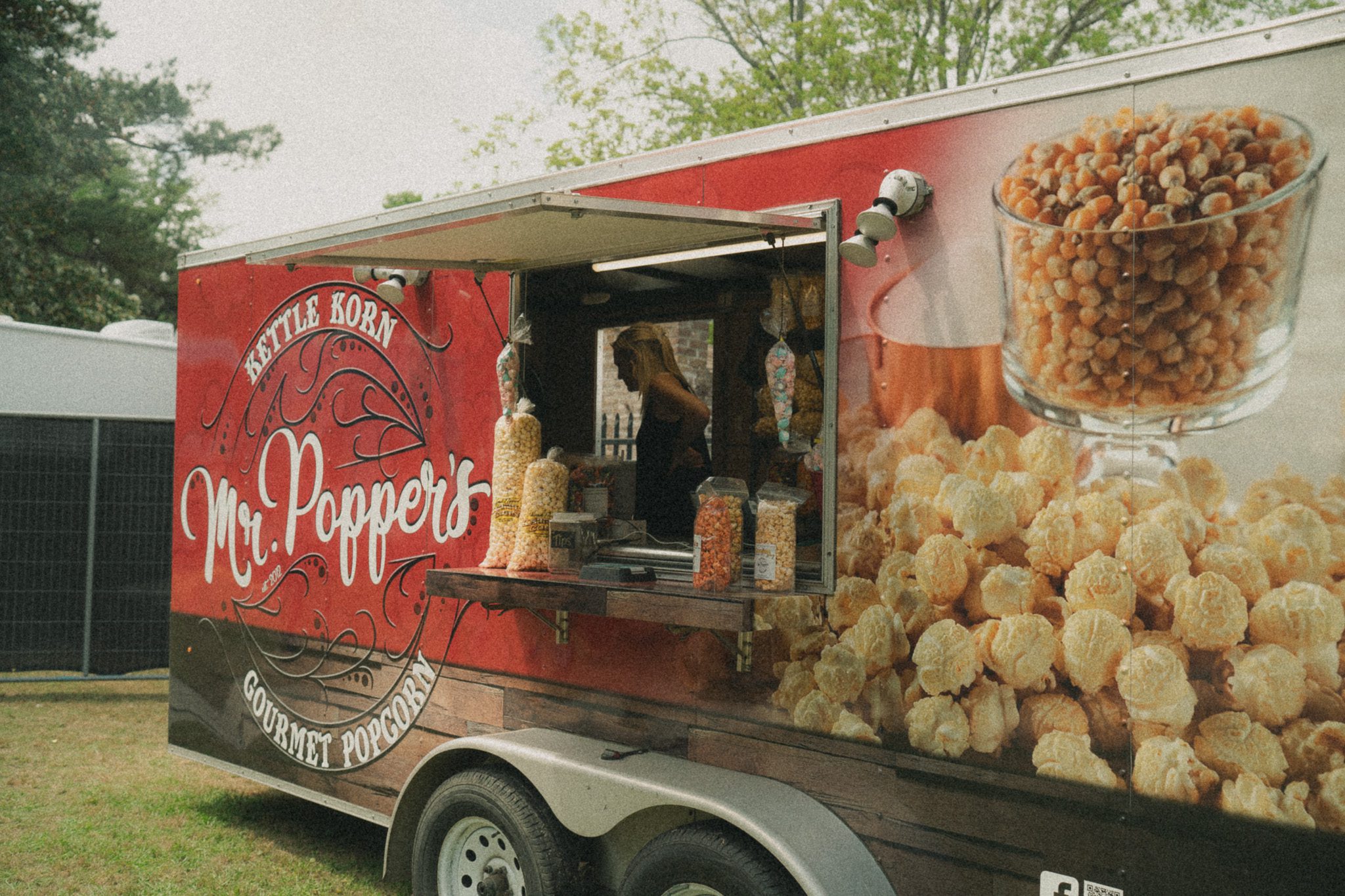 A food trailer with the name 'Mr. Poppers' serving gourmet popcorn, featuring jars of colorful popcorn varieties and kettle corn displayed prominently.