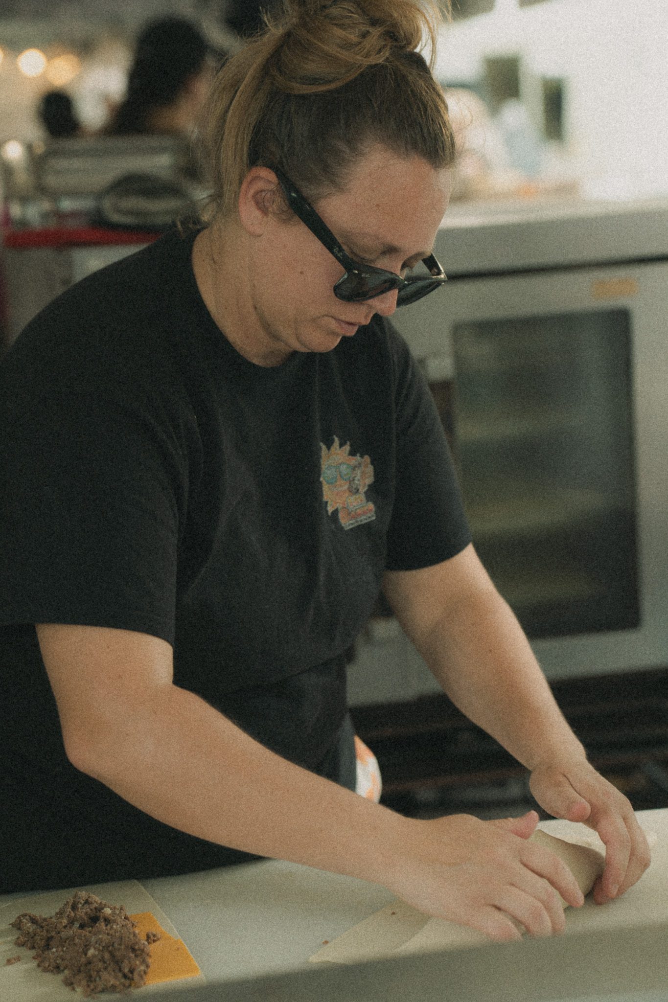 A woman wearing sunglasses prepares food at a festival vendor station, focused on her work.