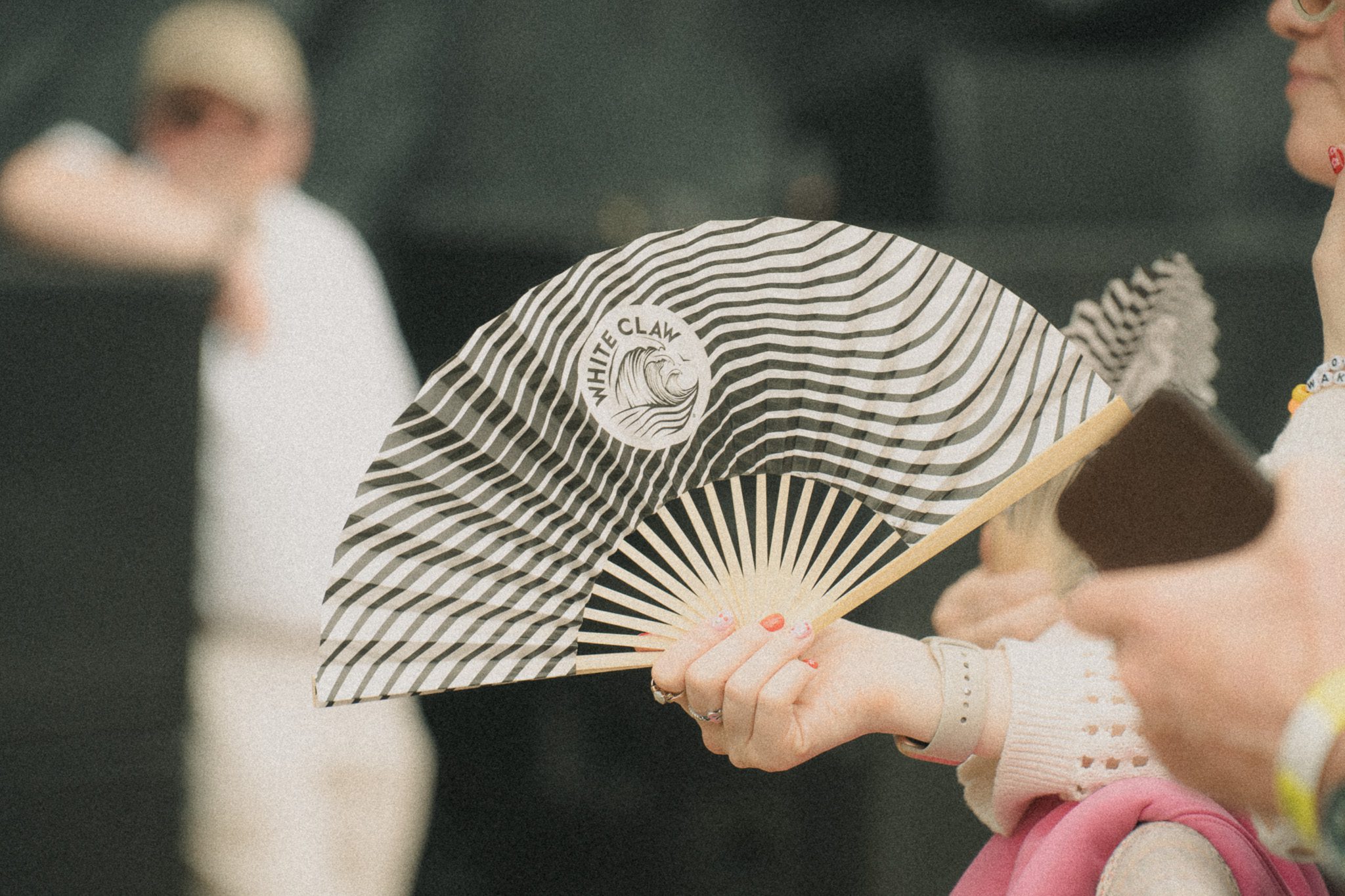 A hand holding a striped fan with a 'White Claw' logo at a festival.