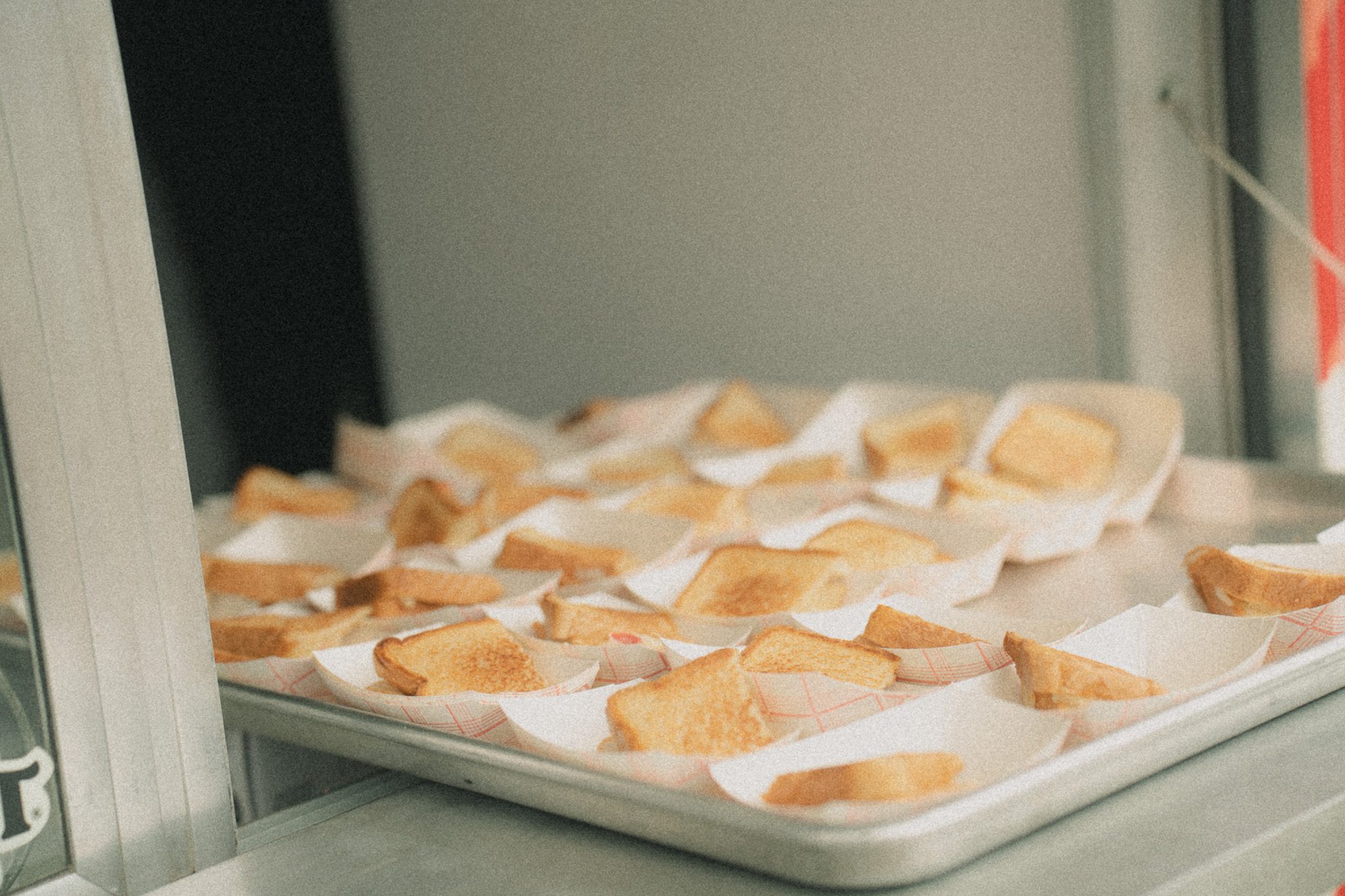 A tray with multiple portions of crispy, toasted bread triangles served in paper holders, likely at a food vendor during a festival.