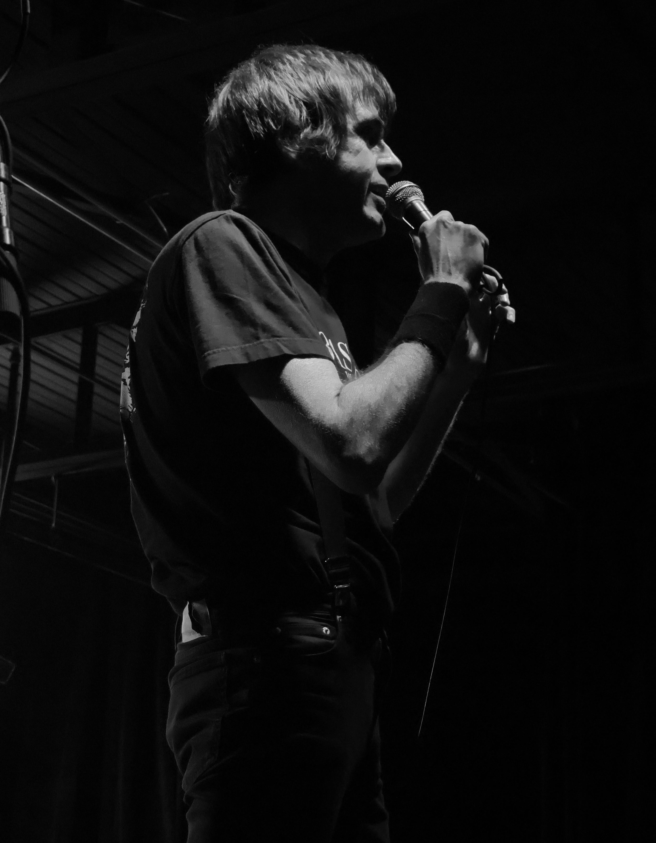 A musician on stage holding a microphone, illuminated by stage lights, in a dark atmosphere.