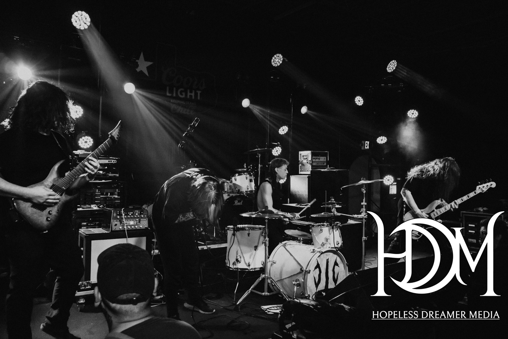 A live performance by a metalcore band featuring guitarists, a drummer, and a vocalist, set against a backdrop of stage lights and equipment.