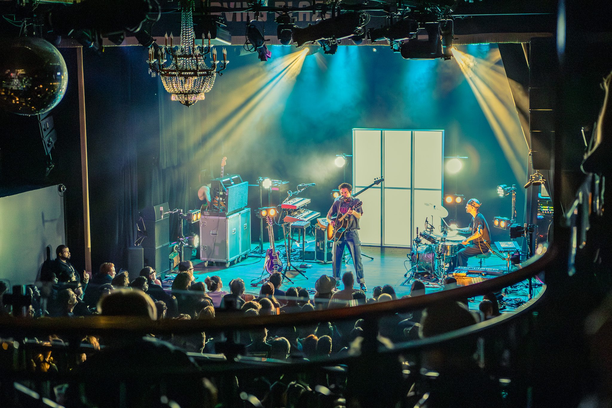 An aerial view of a live music performance at Irving Plaza, featuring Marc Scibilia on stage with a guitarist and drummer, surrounded by various instruments and lighting effects, while an engaged audience watches from below.