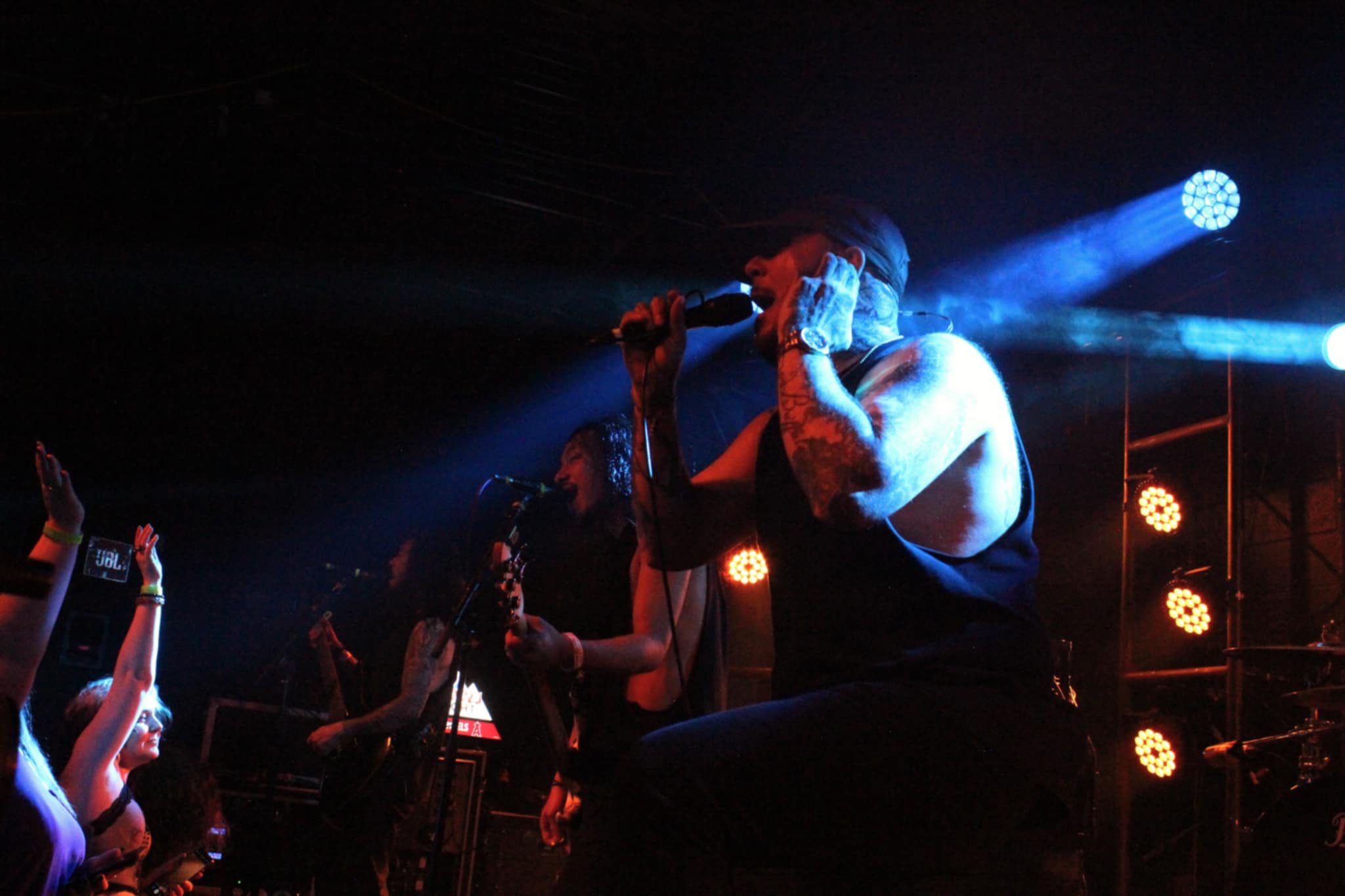 A live performance by a metalcore band with a lead singer passionately engaging the audience, surrounded by band members and dramatic stage lighting.