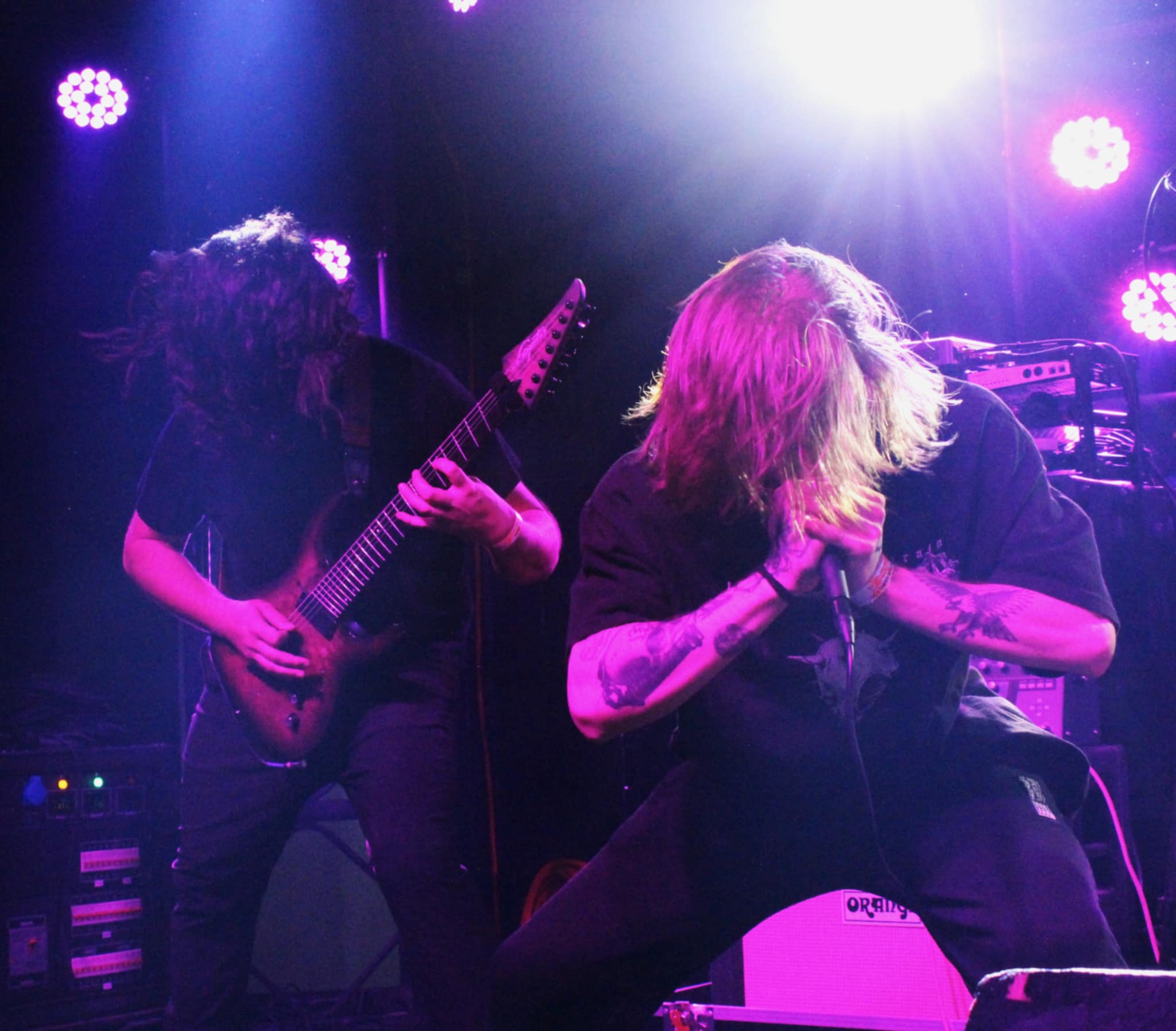 A metalcore band performing live on stage with dynamic lighting, featuring a guitarist playing passionately and a vocalist expressing intense emotion.