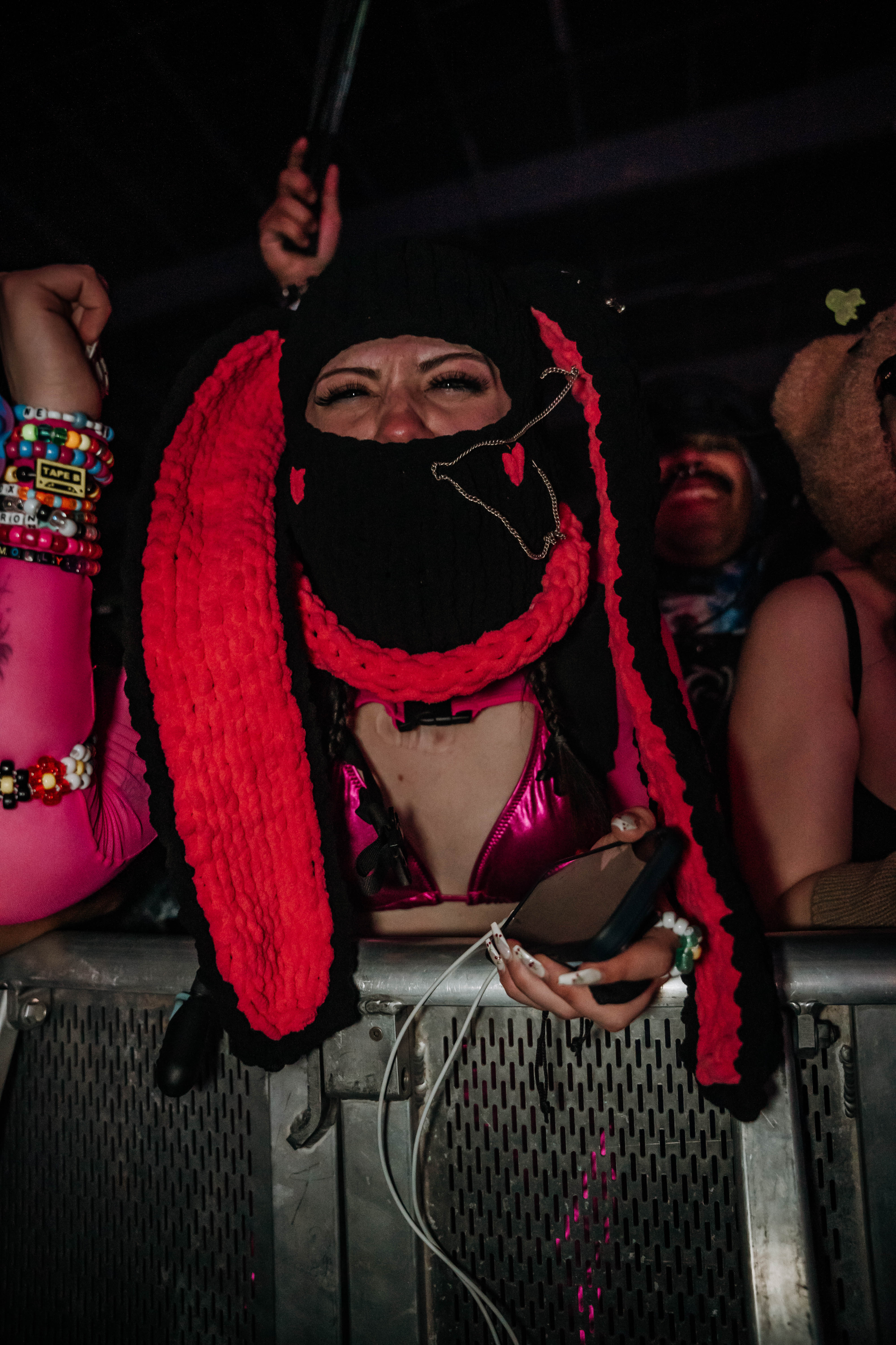 A festival-goer dressed in a vibrant outfit and unique, knitted headgear with long ears, eagerly enjoying the performance. The crowd is lively in the background, embodying the energetic atmosphere of the event.