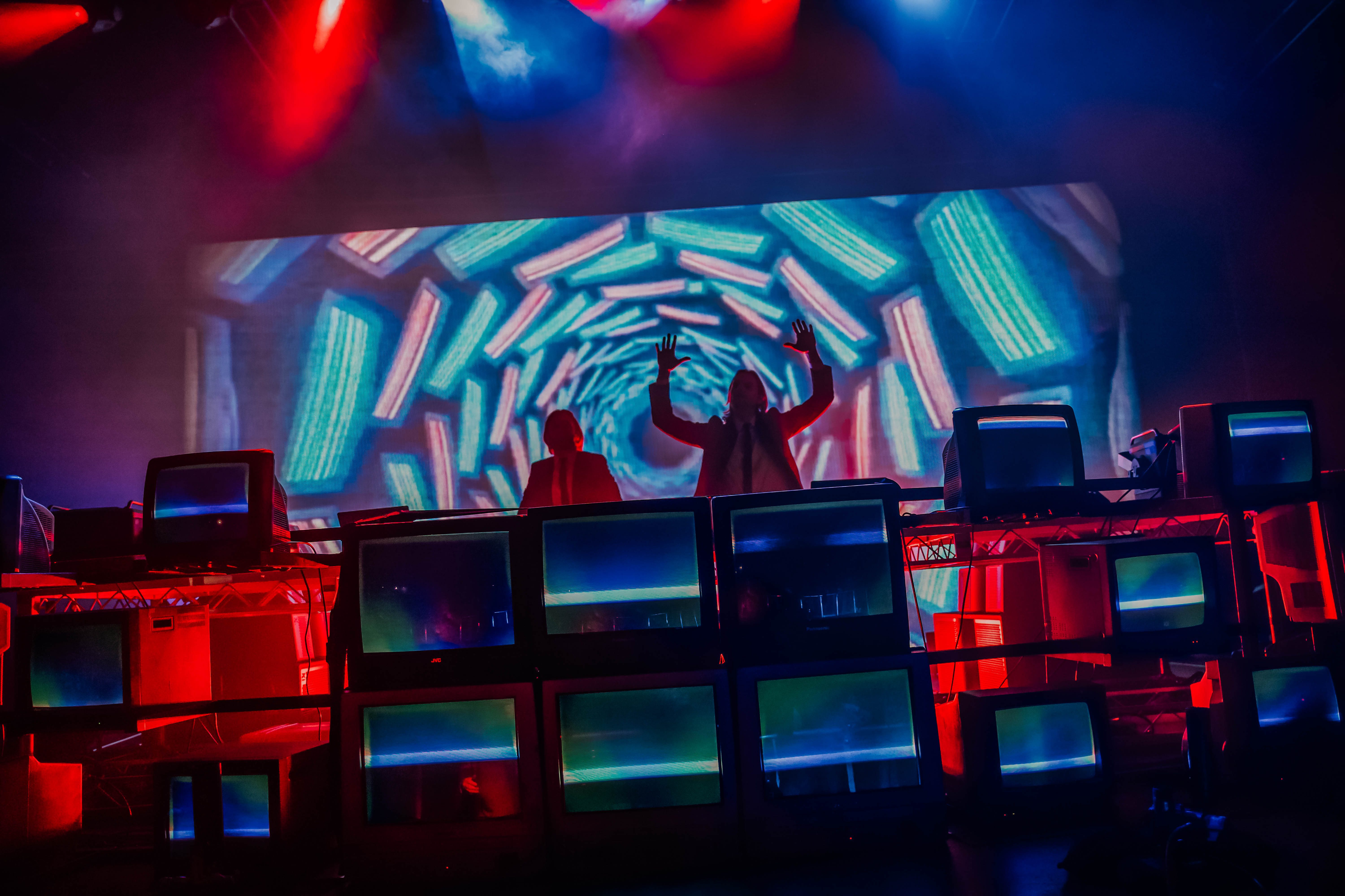 A dynamic performance by Zeds Dead at Rawhide, featuring two DJs in front of a backdrop of vintage TVs and vibrant visual displays, illuminated by red and blue lights.