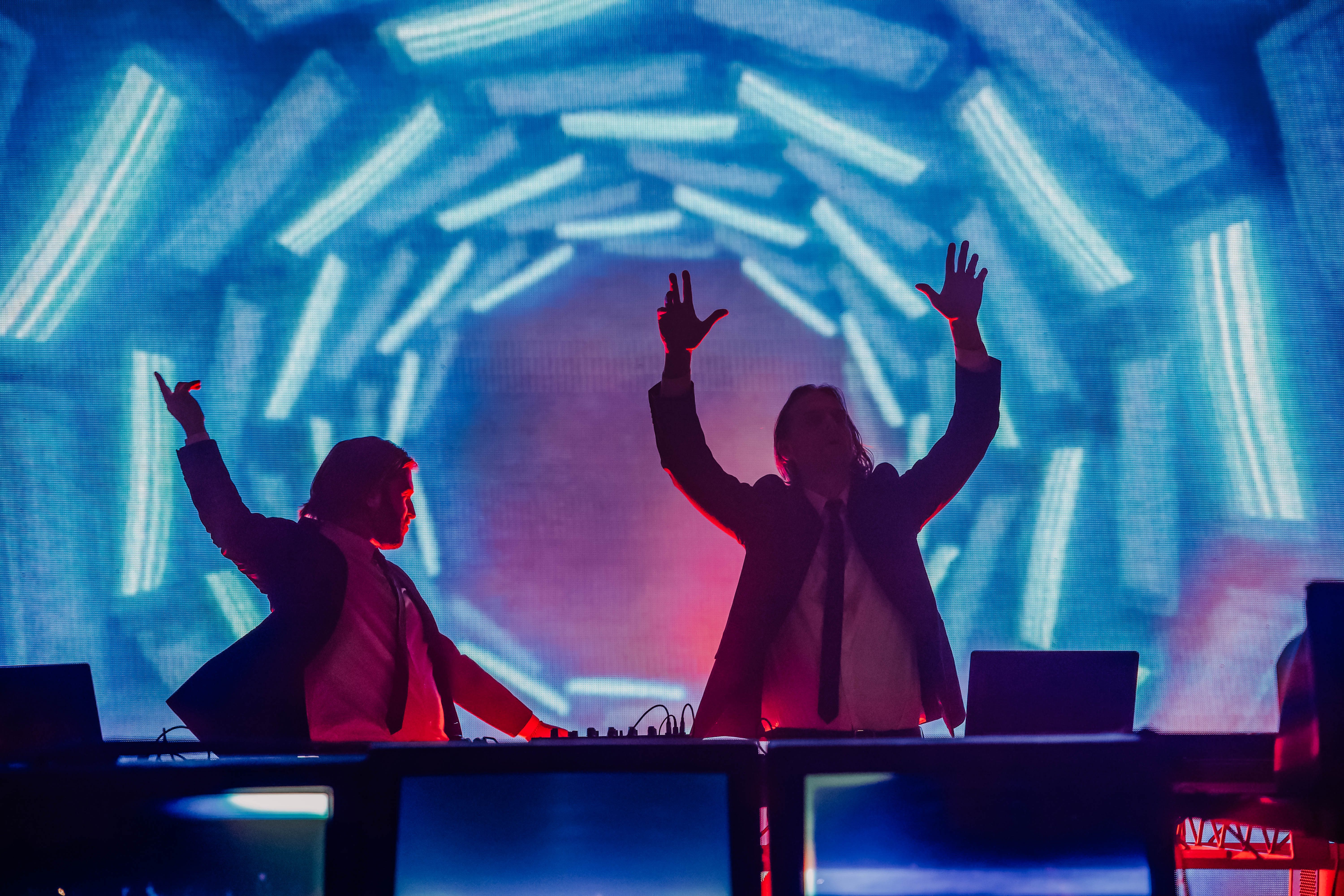 Two DJs perform on stage against a backdrop of vibrant, swirling lights, showcasing an energetic atmosphere at a music concert.