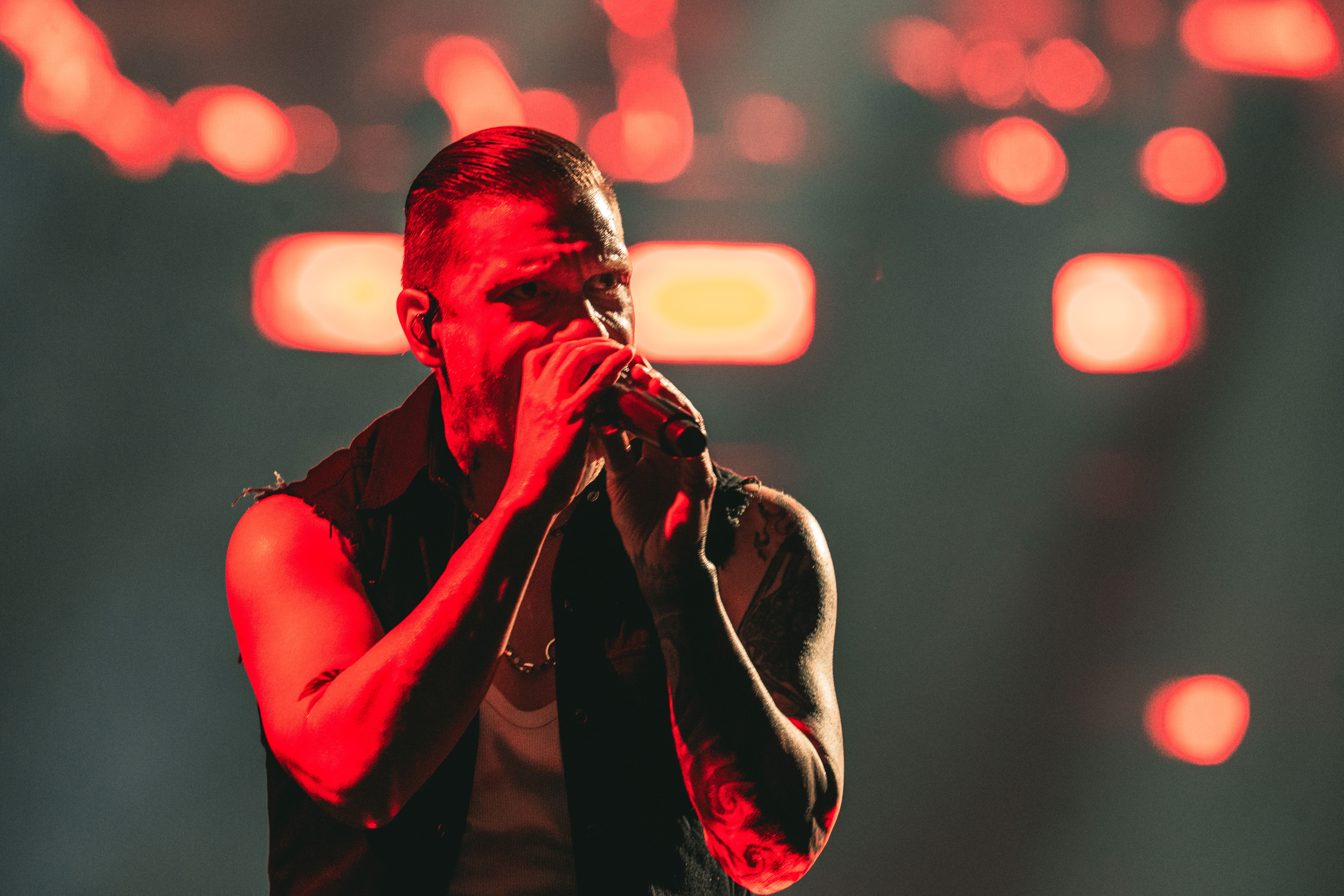 A male singer passionately performing on stage with a microphone, illuminated by red stage lights.