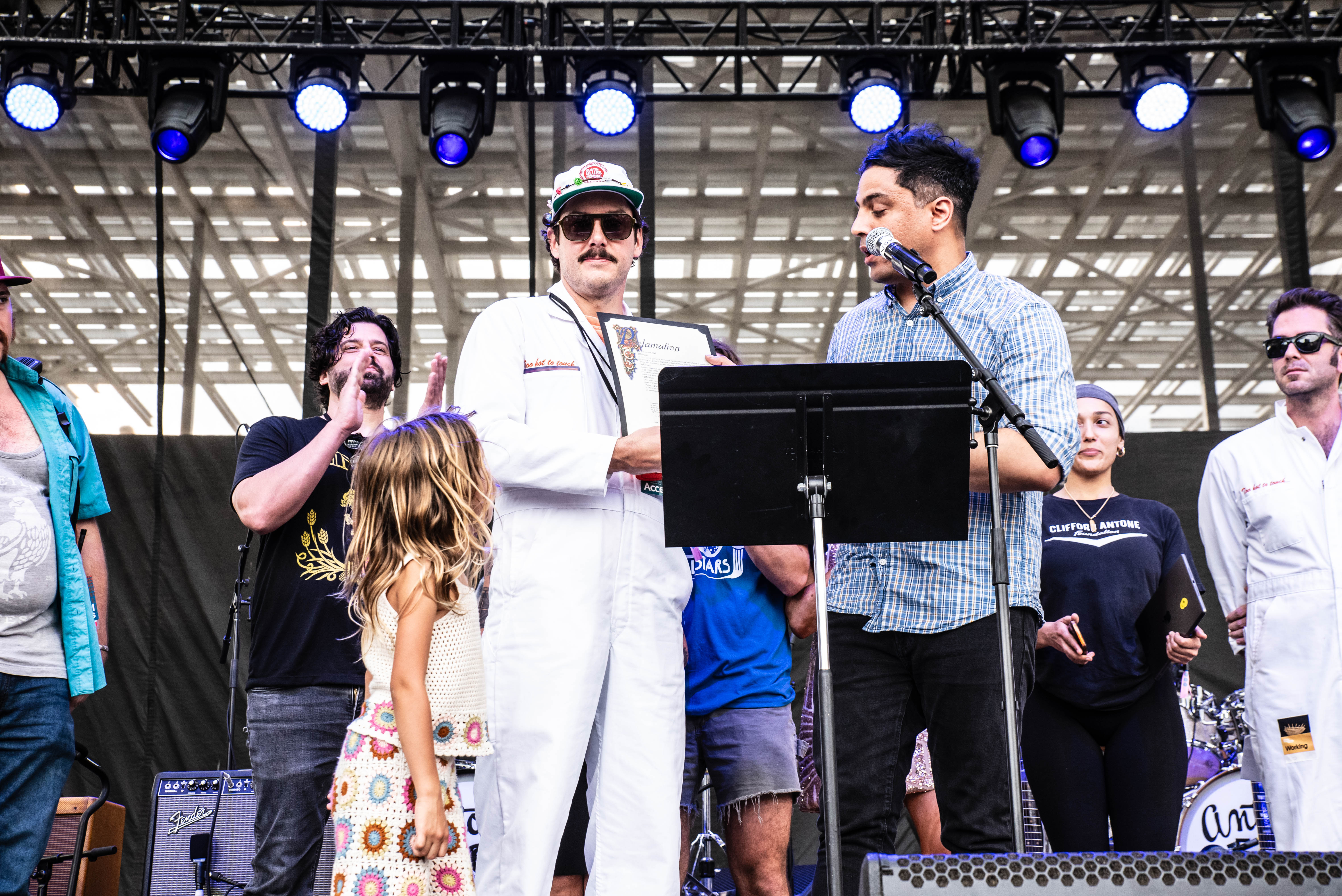 A group of people on stage at a music festival, with one person holding a framed document, while others celebrate and applaud.