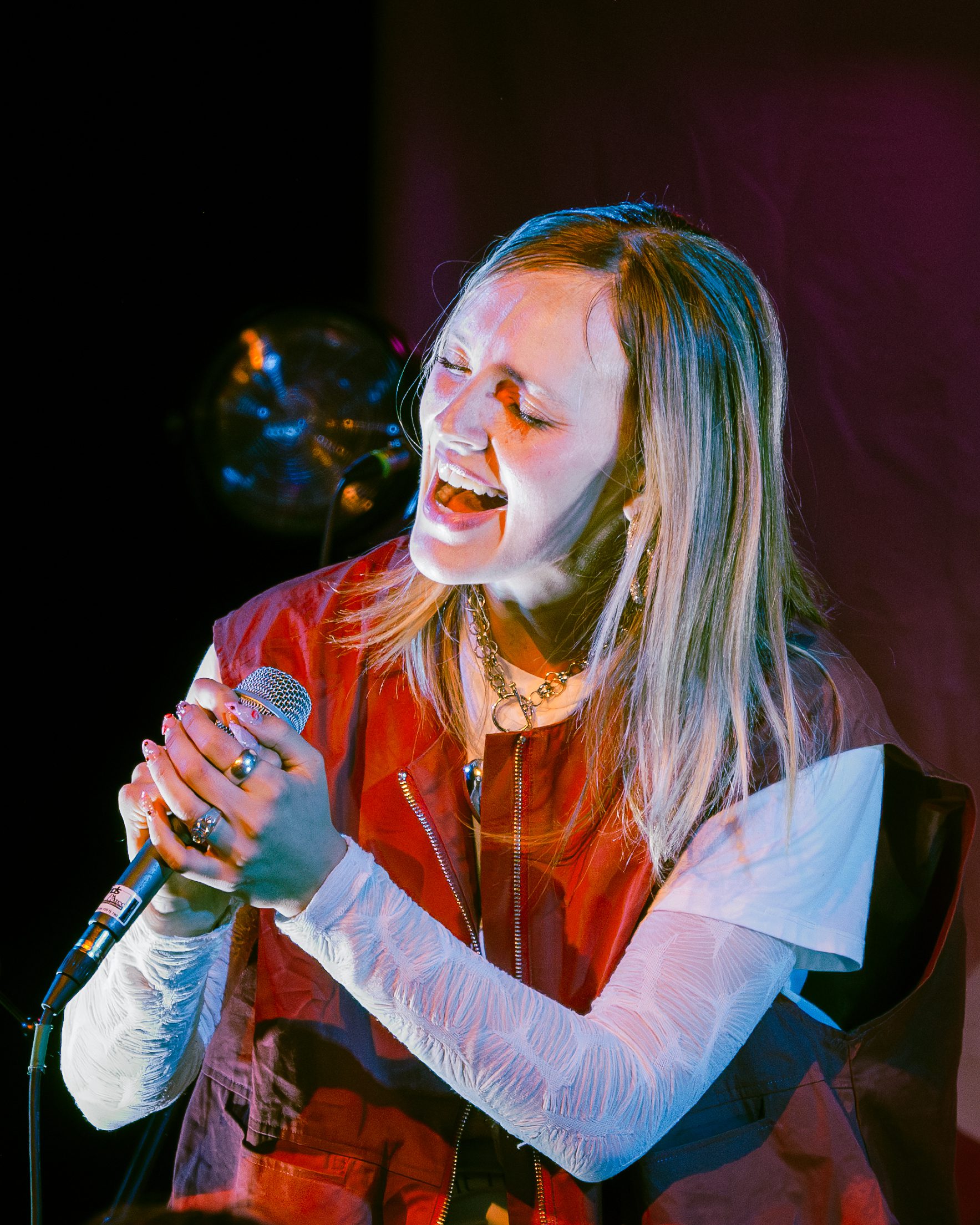 A singer passionately performing on stage, holding a microphone and singing with an expressive facial expression.