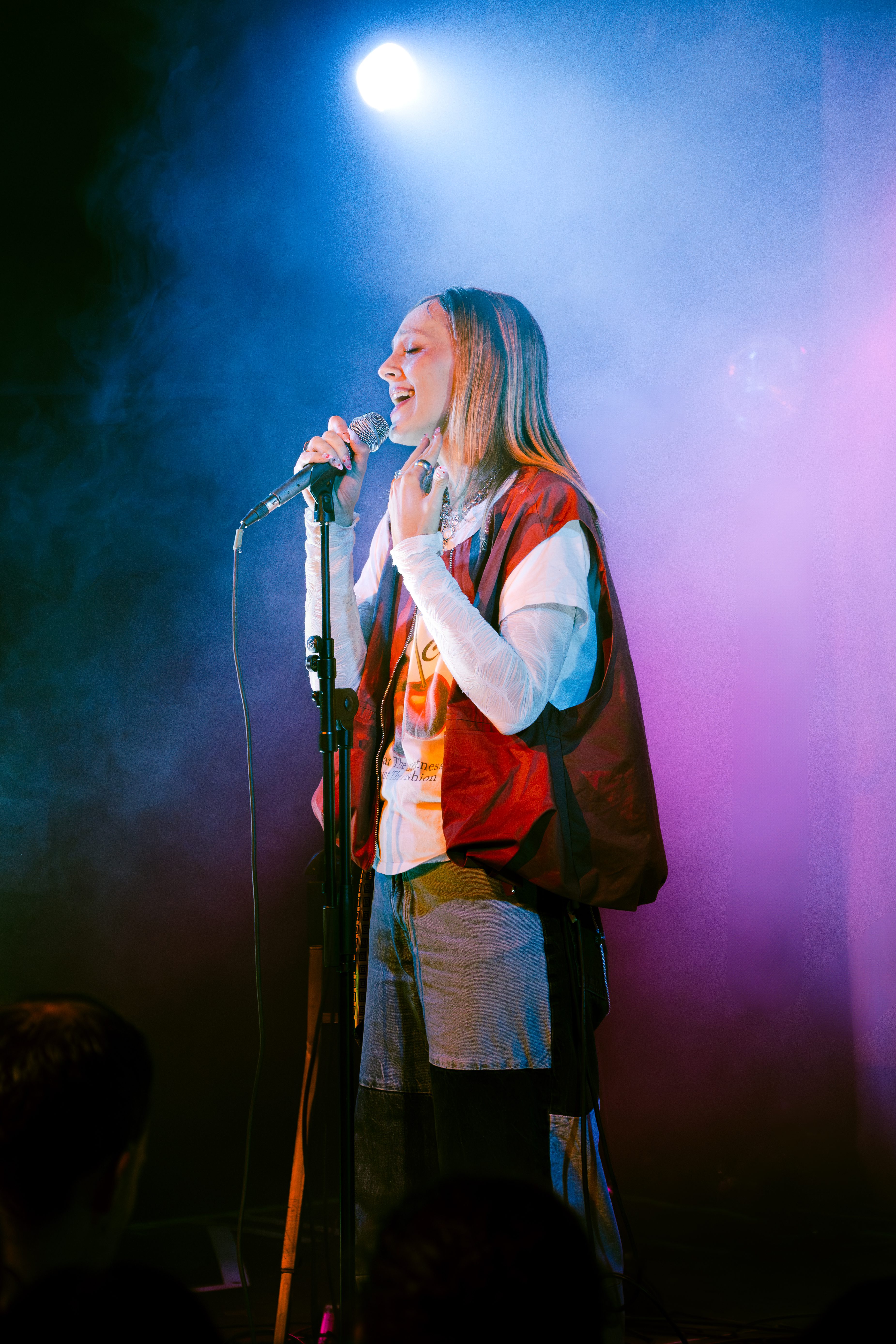 A young woman singing into a microphone on stage, surrounded by colorful lighting and smoke.