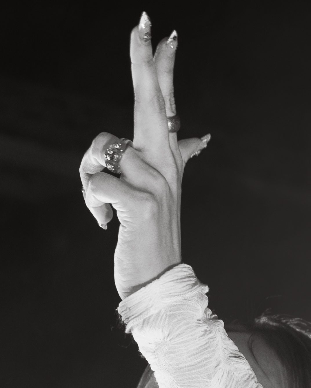 A close-up of a hand making a peace sign, adorned with rings, set against a dark background.
