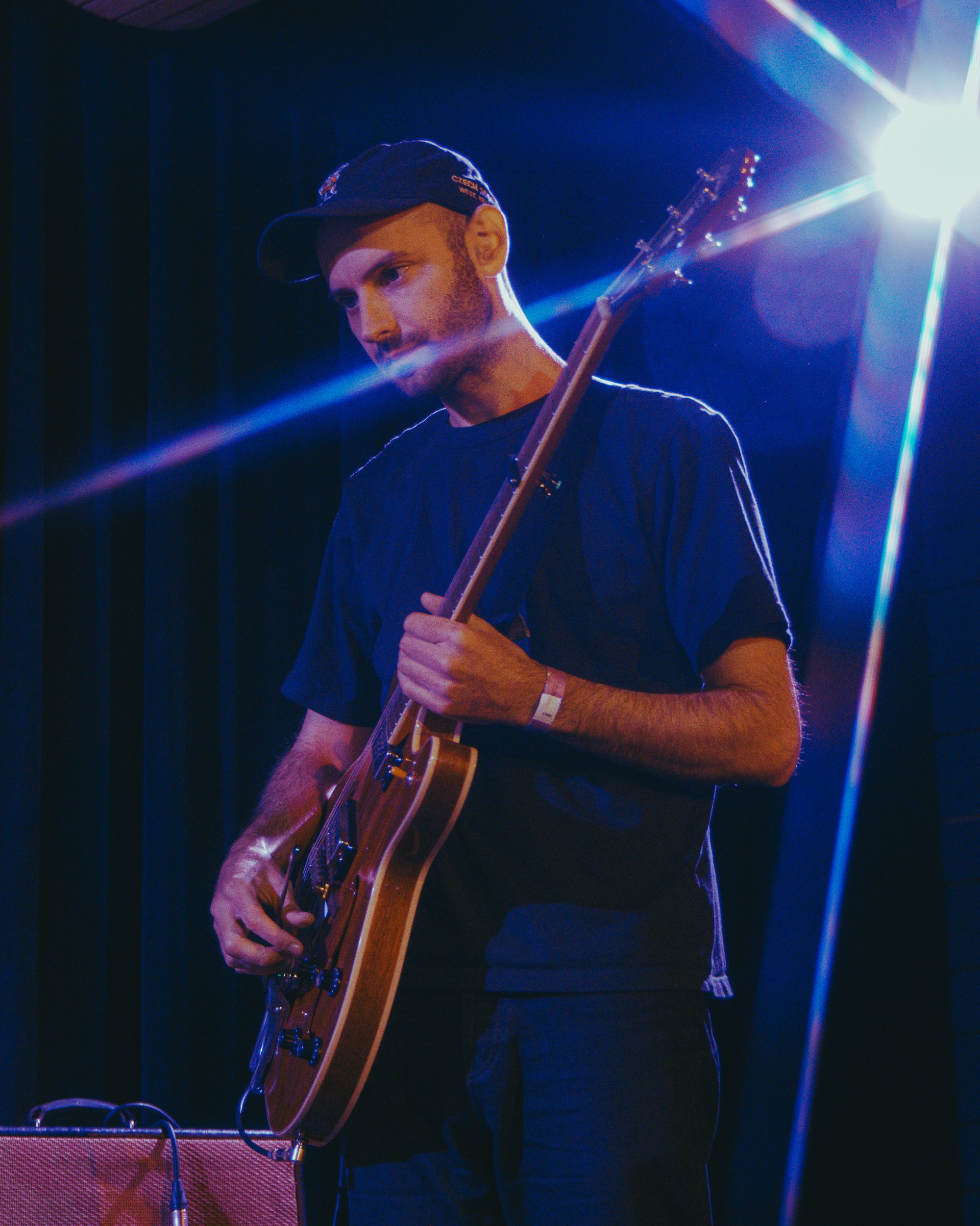A musician holding a guitar on stage, illuminated by soft lighting, with a focused expression.