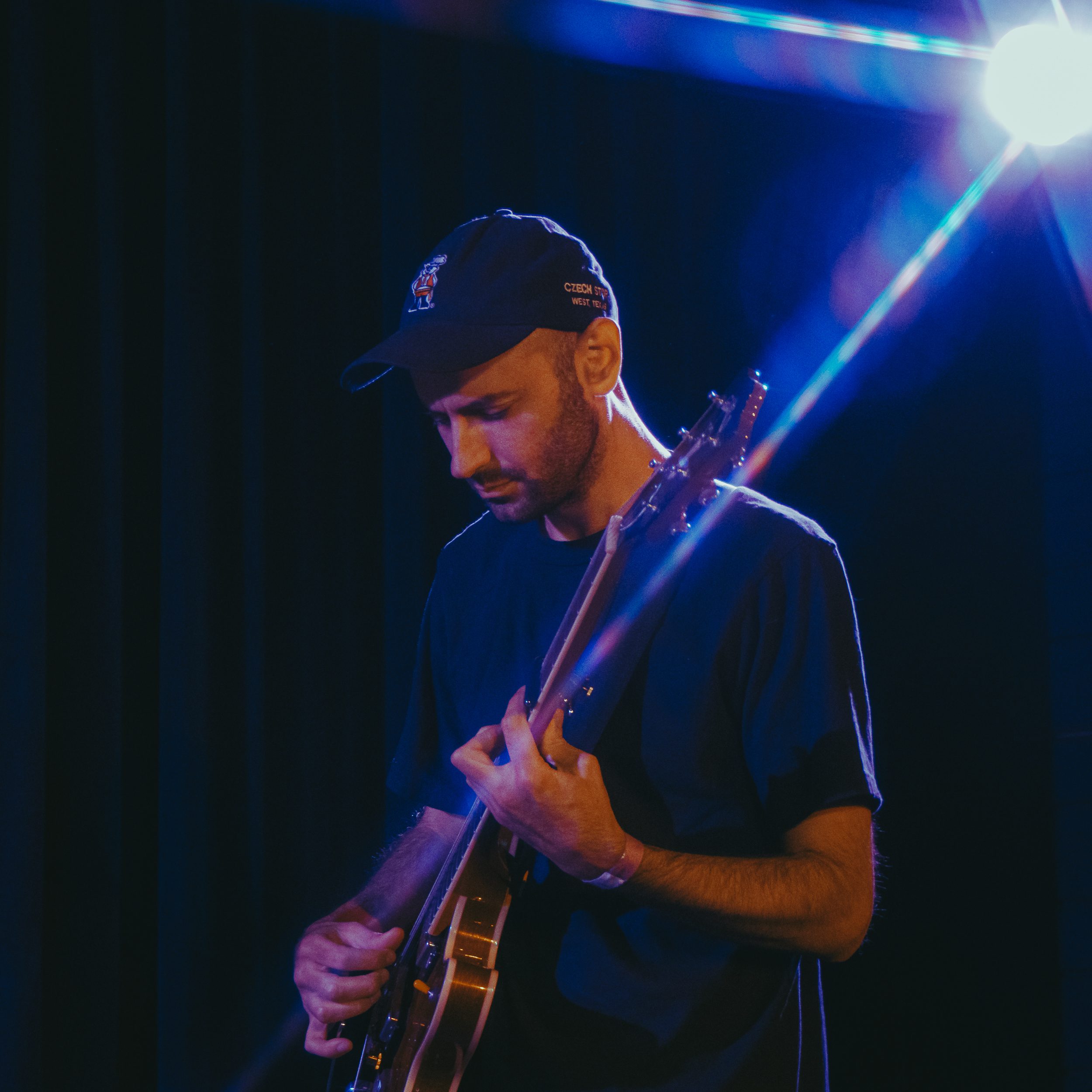 A musician playing guitar on stage, focused and immersed in performance, with soft blue lighting in the background.