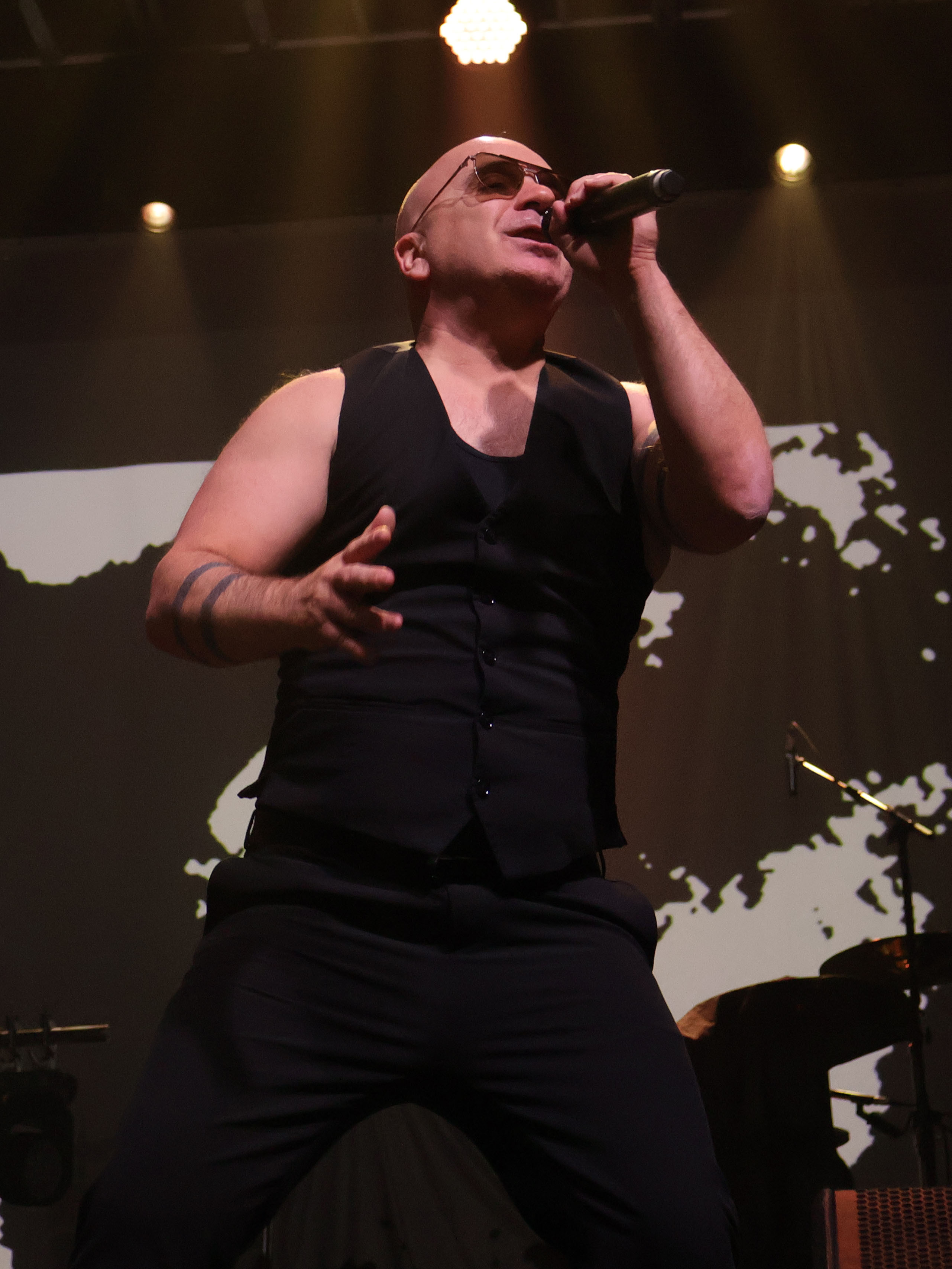A singer performing on stage under dramatic lighting, wearing sunglasses and a black outfit, passionately engaging with the audience.