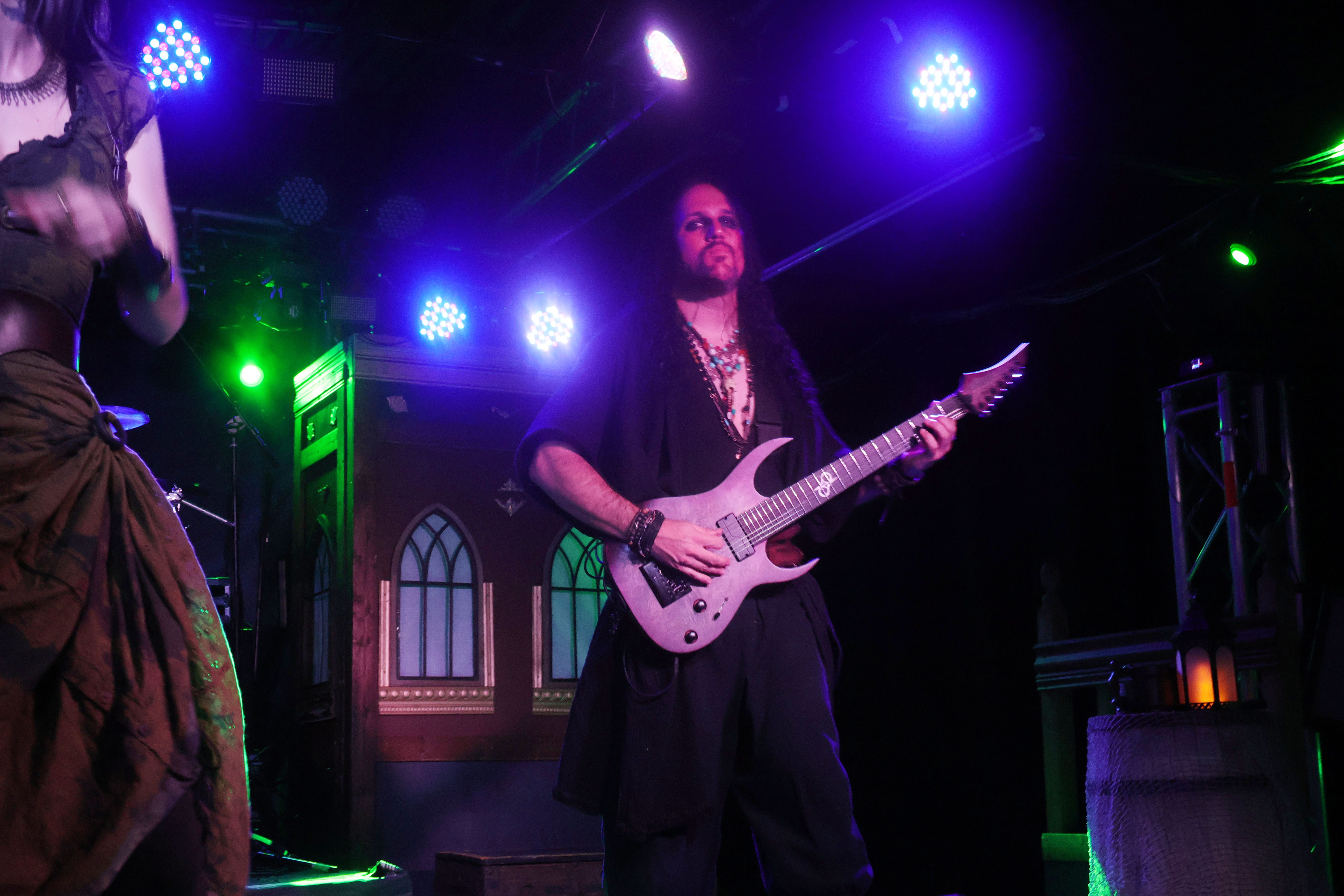A guitarist performing on stage with dramatic lighting during a live music event, wearing a pirate-themed outfit.