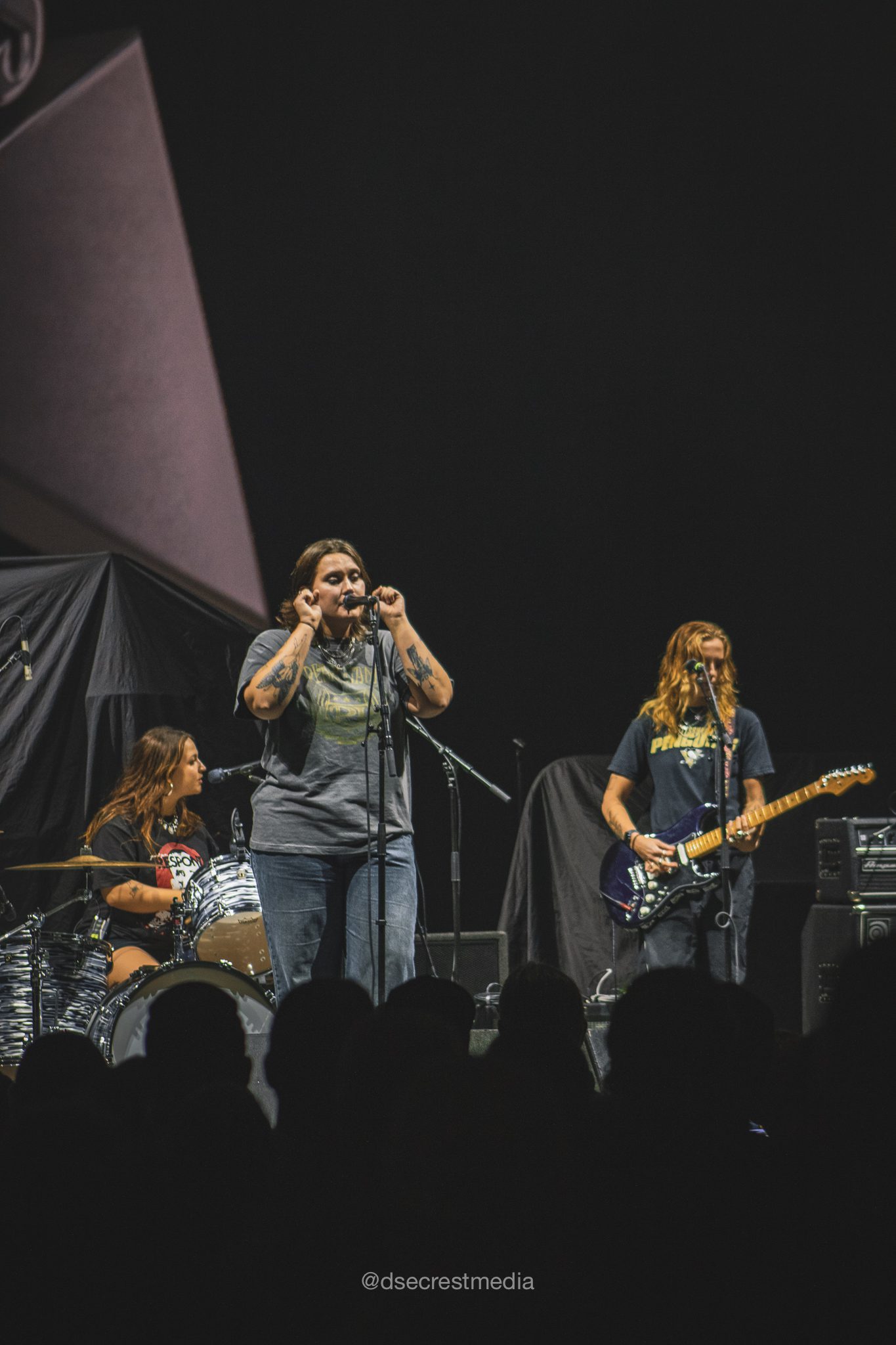 An all-female punk-rock band performing on stage with a drummer and two guitarists, engaging the audience during a live concert.