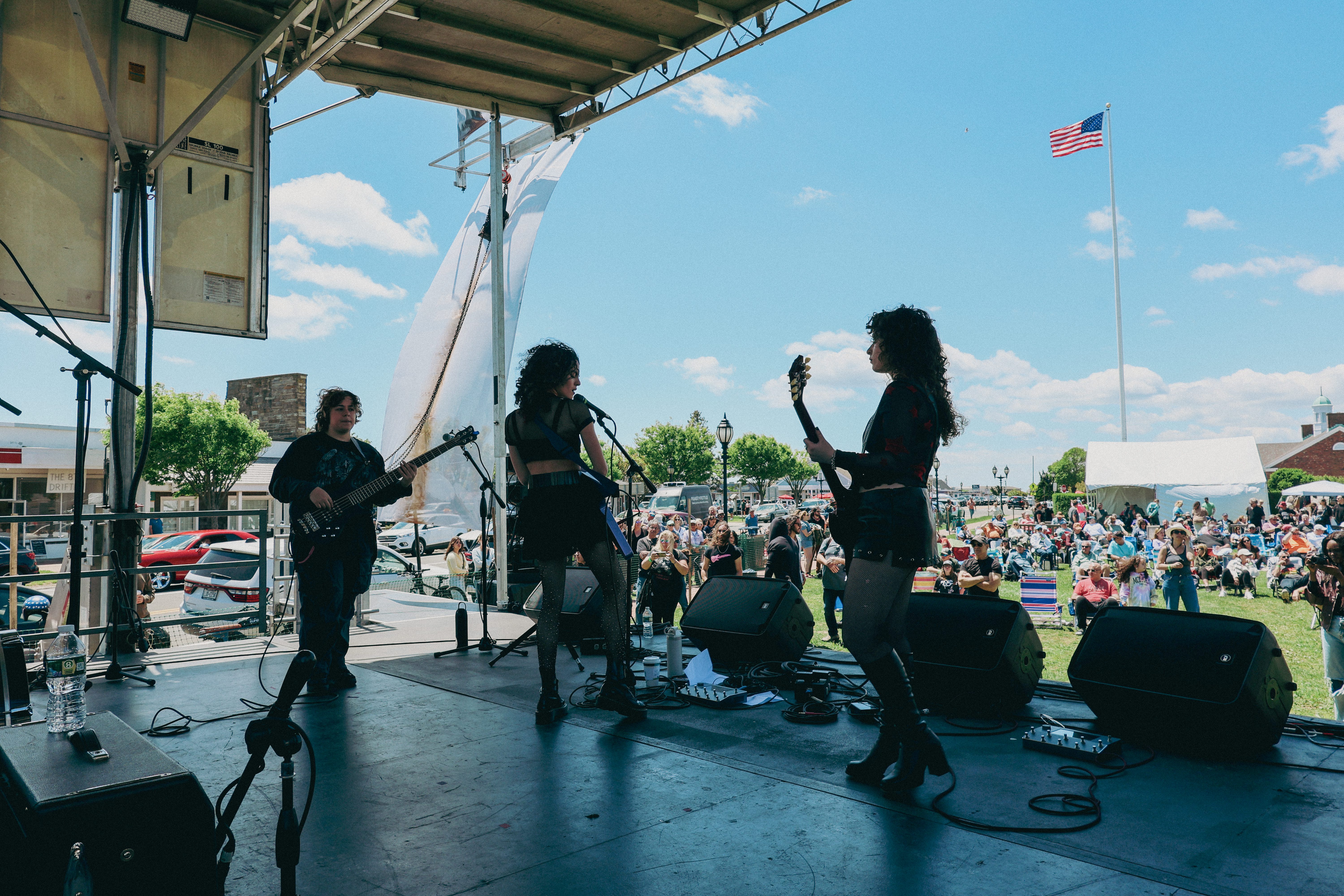 A band performing on stage at the Montauk Music Festival, with a crowd enjoying the show in the background on a sunny day.