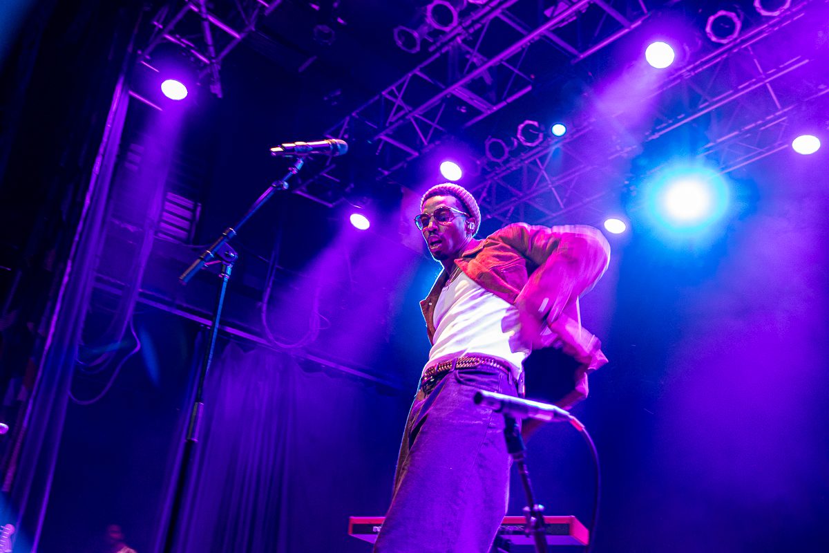 Anees performing live on stage with vibrant purple lighting and a microphone, engaging with the audience.