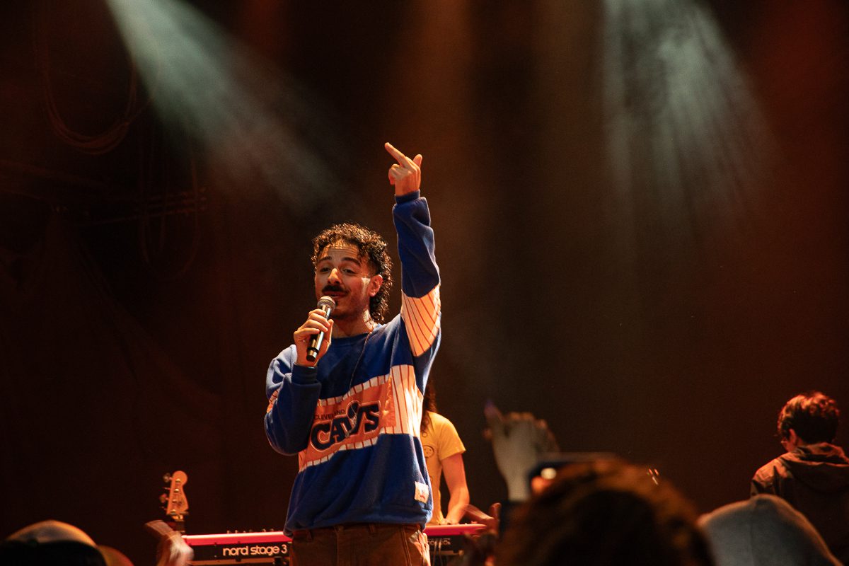 Anees performing on stage at the House of Blues in Cleveland, Ohio, wearing a blue sweater and holding a microphone while engaging with the crowd.
