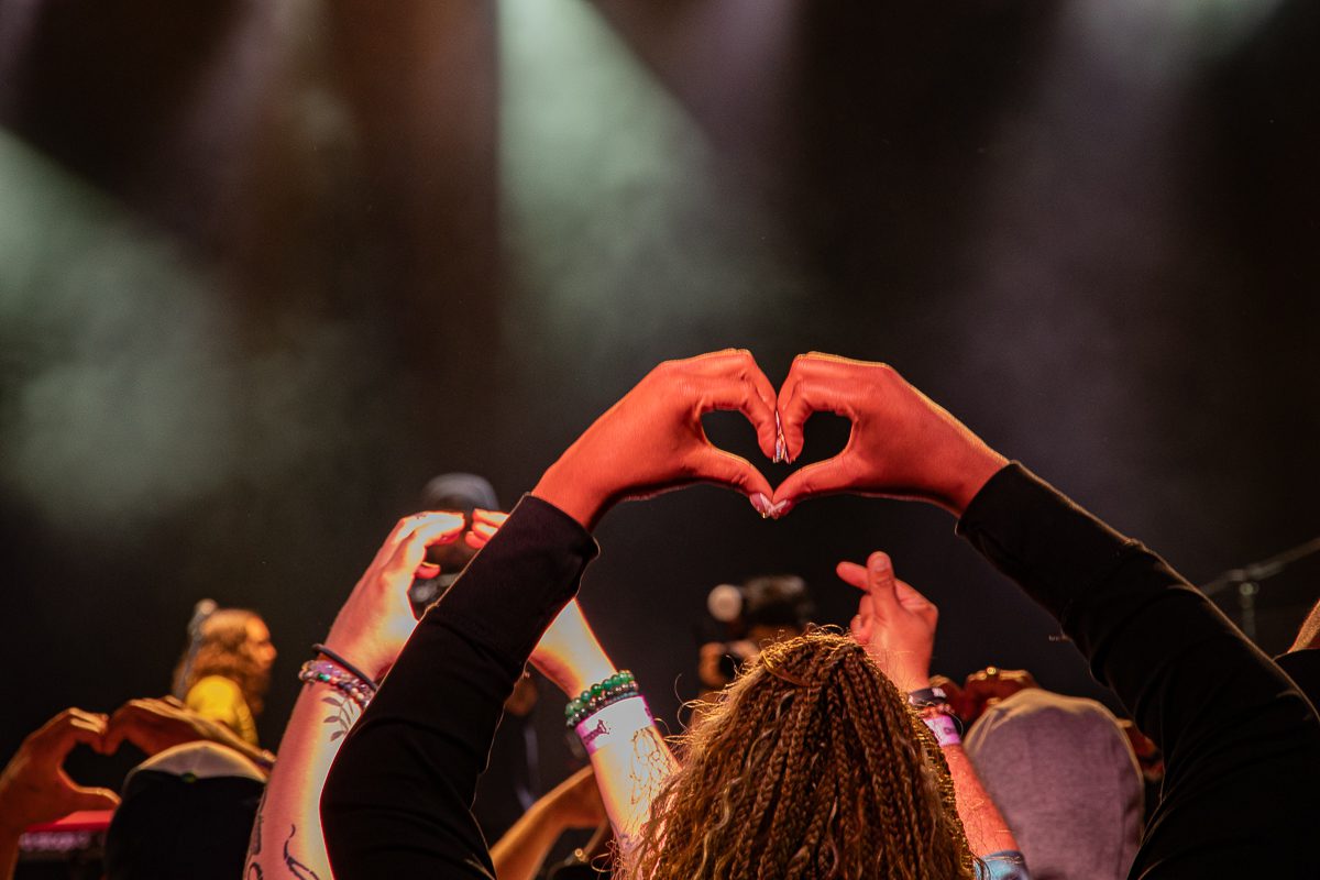 Audience members forming heart shapes with their hands during a live music performance, capturing the connection and excitement in the atmosphere.