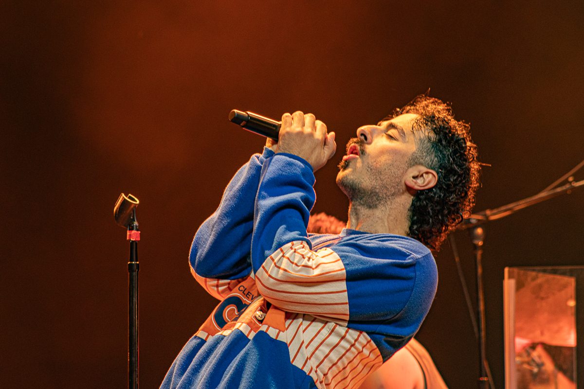Anees performing on stage, singing passionately into the microphone while wearing a colorful sweater.