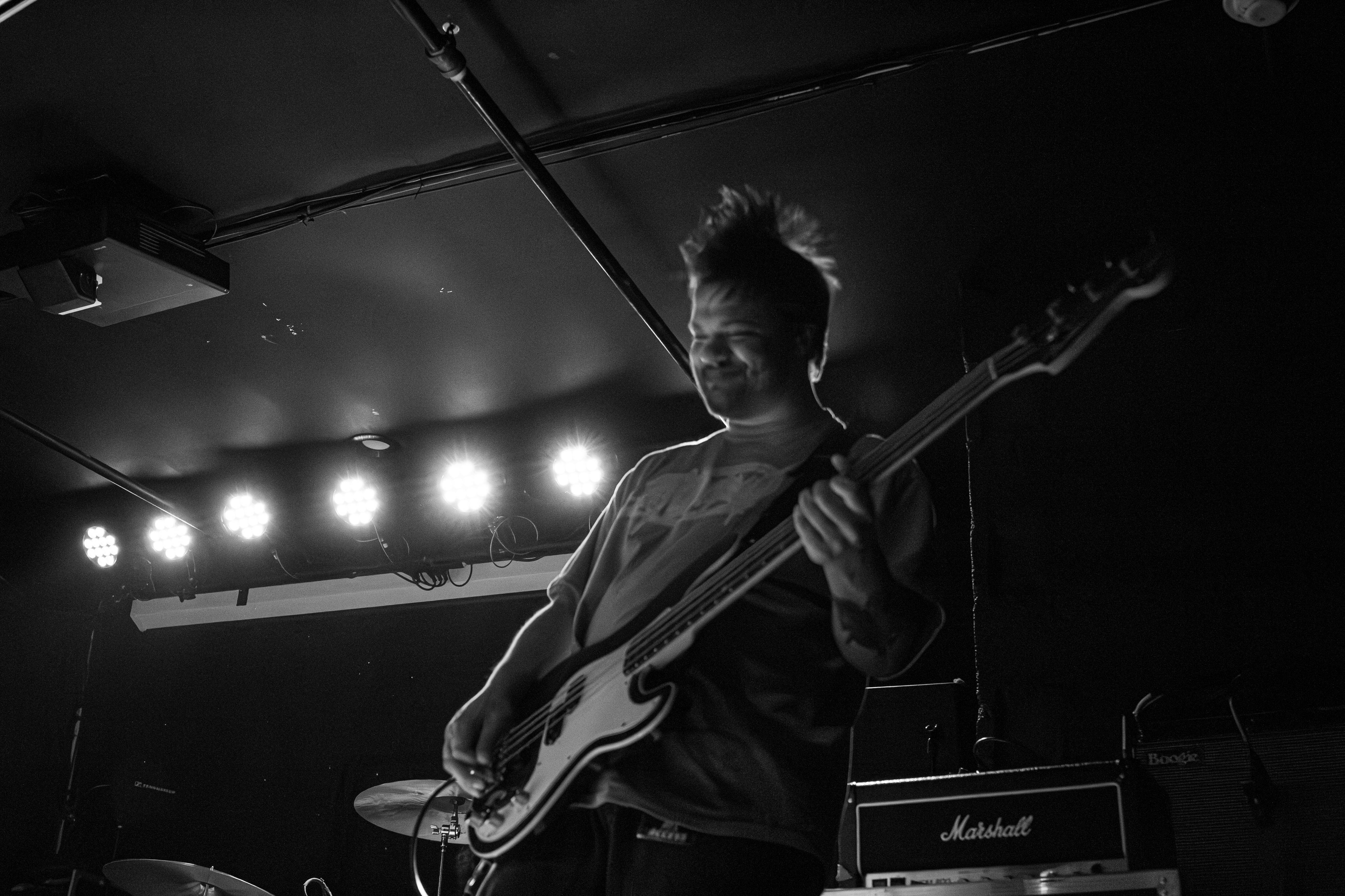 A musician joyfully playing bass guitar on stage, under bright stage lights.