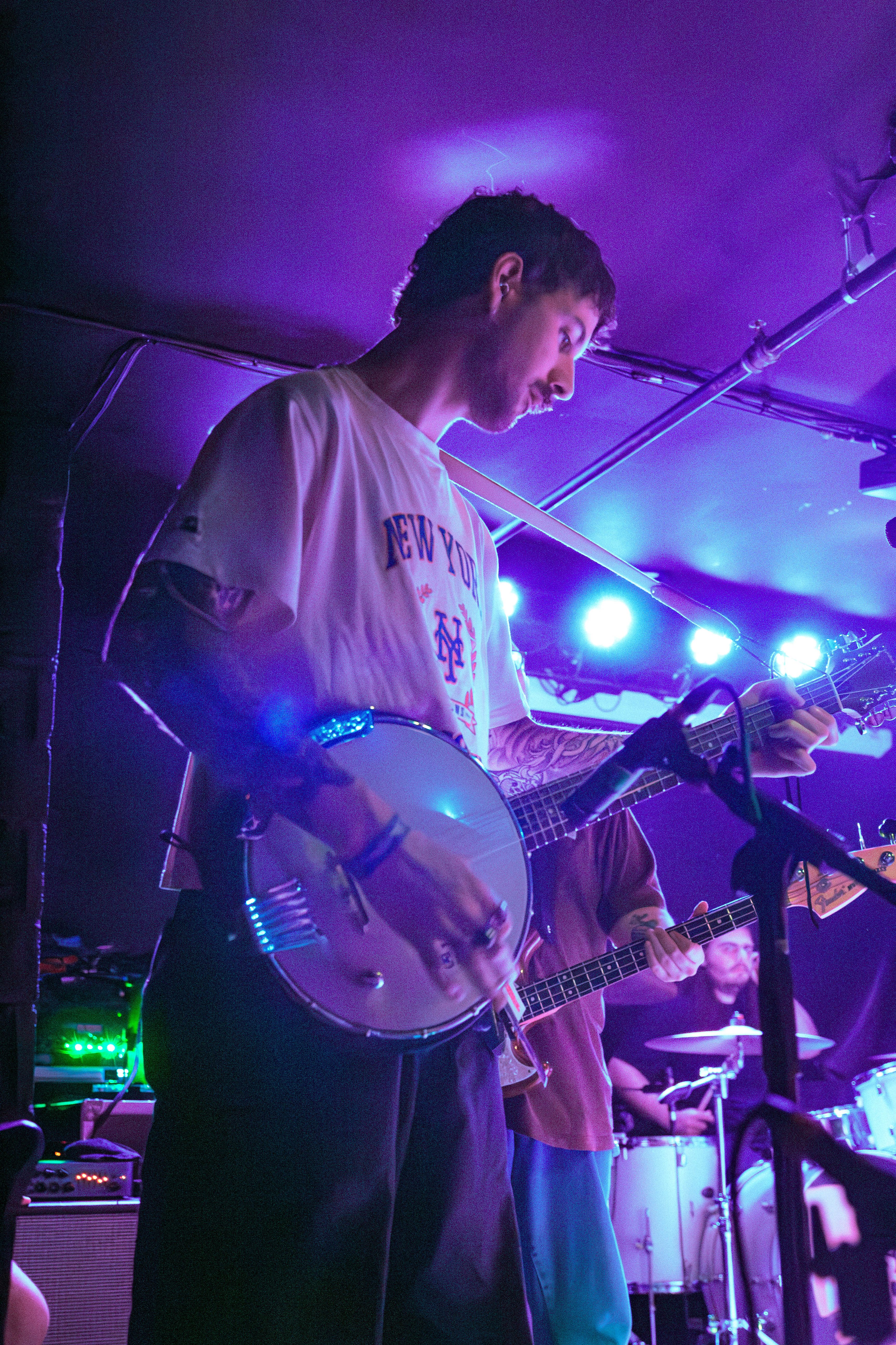 A performer playing a banjo on stage with colorful lighting in the background during a live music event.