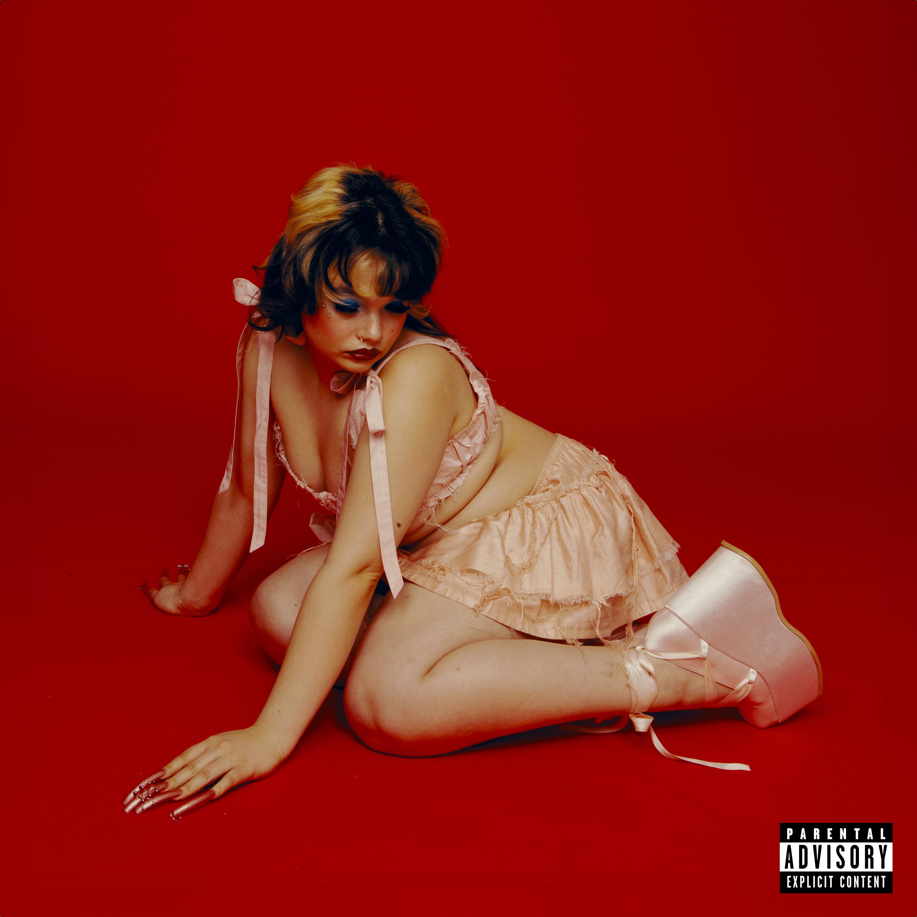 Lola Young posing in a pink outfit with bows against a vibrant red background, showcasing her bold fashion and artistic expression.